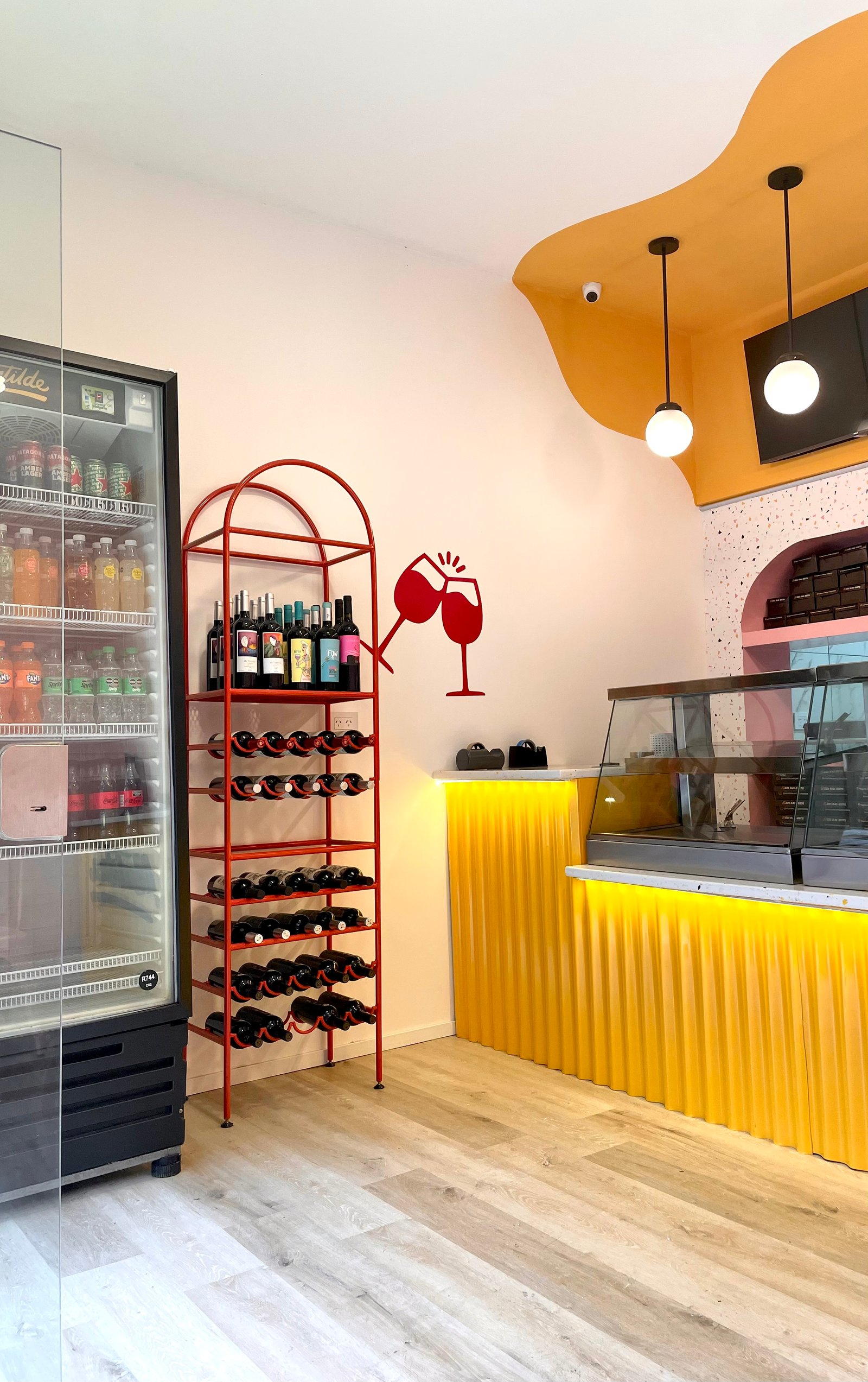 Local comercial con estanterías de vino rojas y mostrador amarillo — proyecto Matilde Empanadas, por ACH Architecture, en La Plata