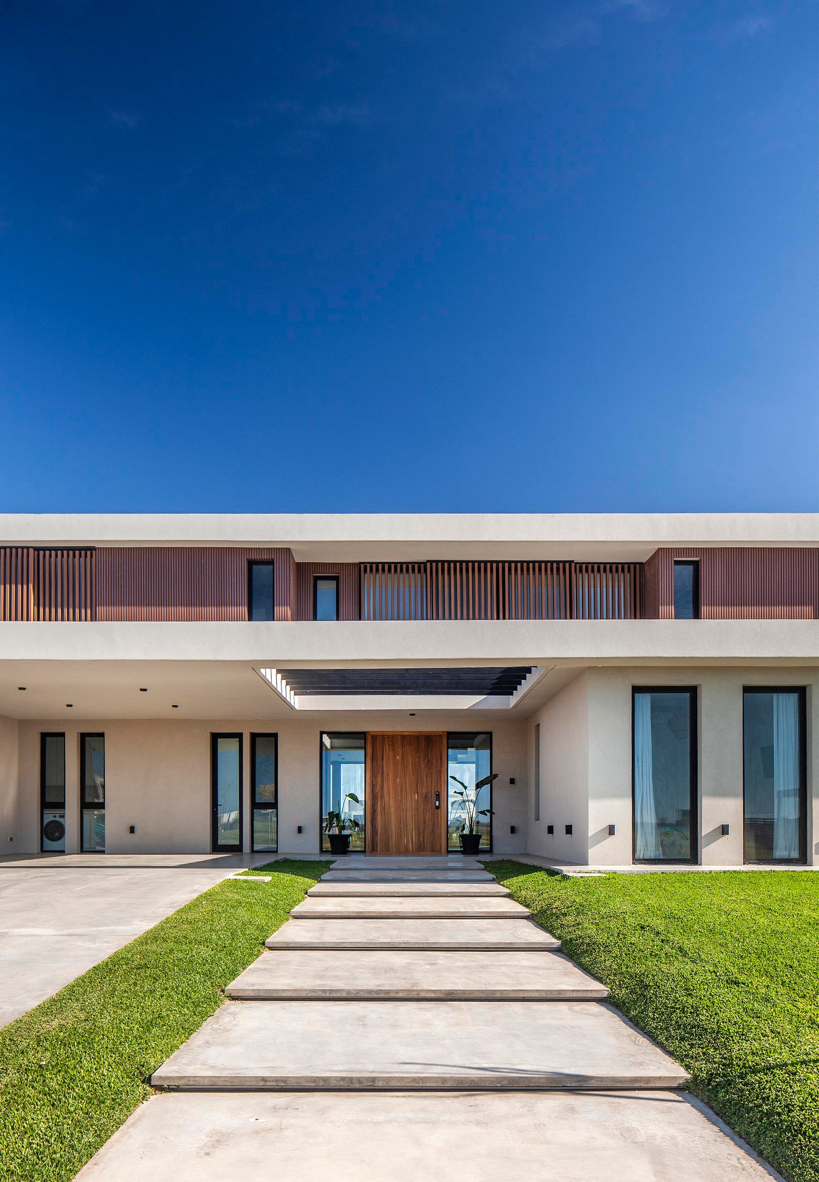 fachada moderna con detalles de madera y grandes ventanales — proyecto CASA C313, por A'PRIMA - Arquitectura Sustentable, en Provincia de Buenos Aires