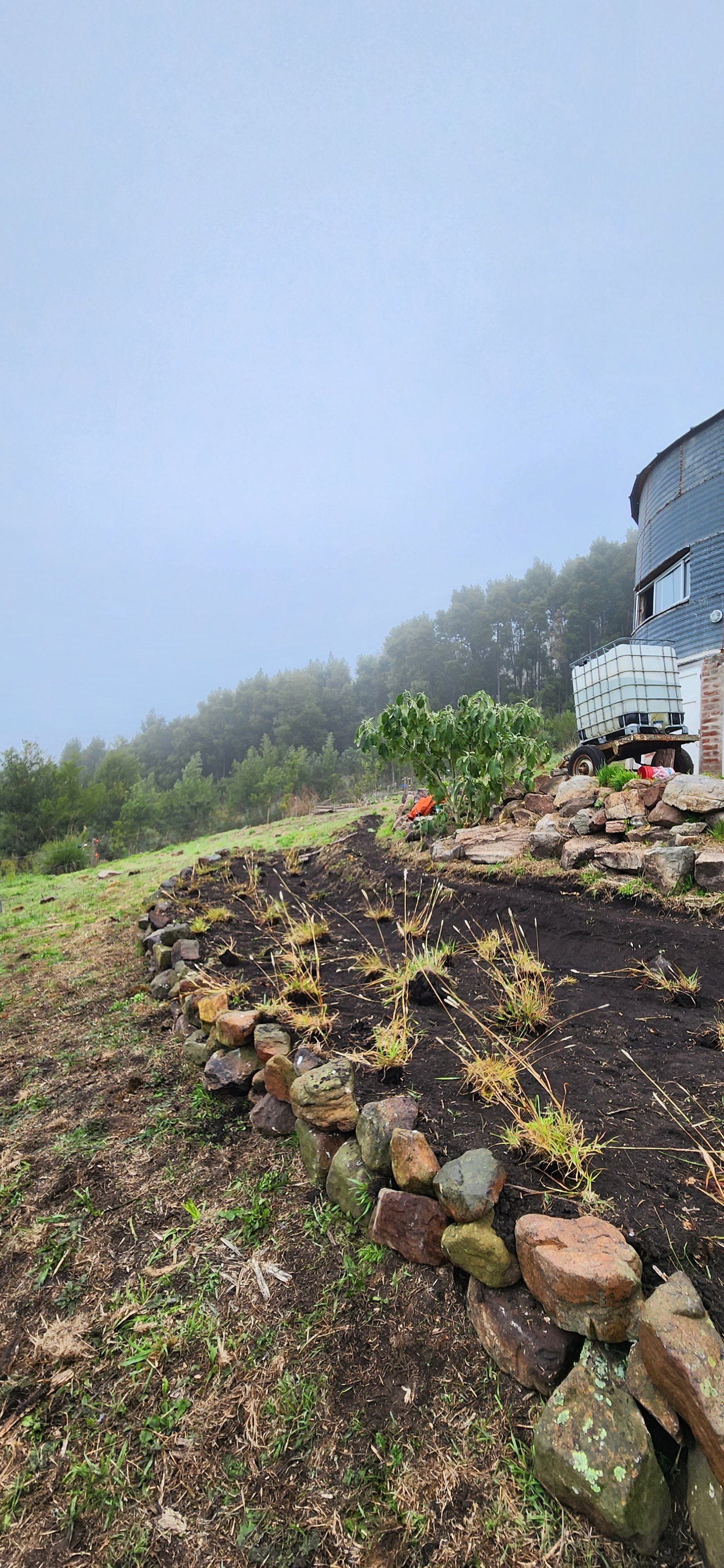 Terreno rural con muro de piedra en construcción y tanque de agua — proyecto Reserva Naural Paititi, por Estudio Rifahi, en Sierra de los Padres