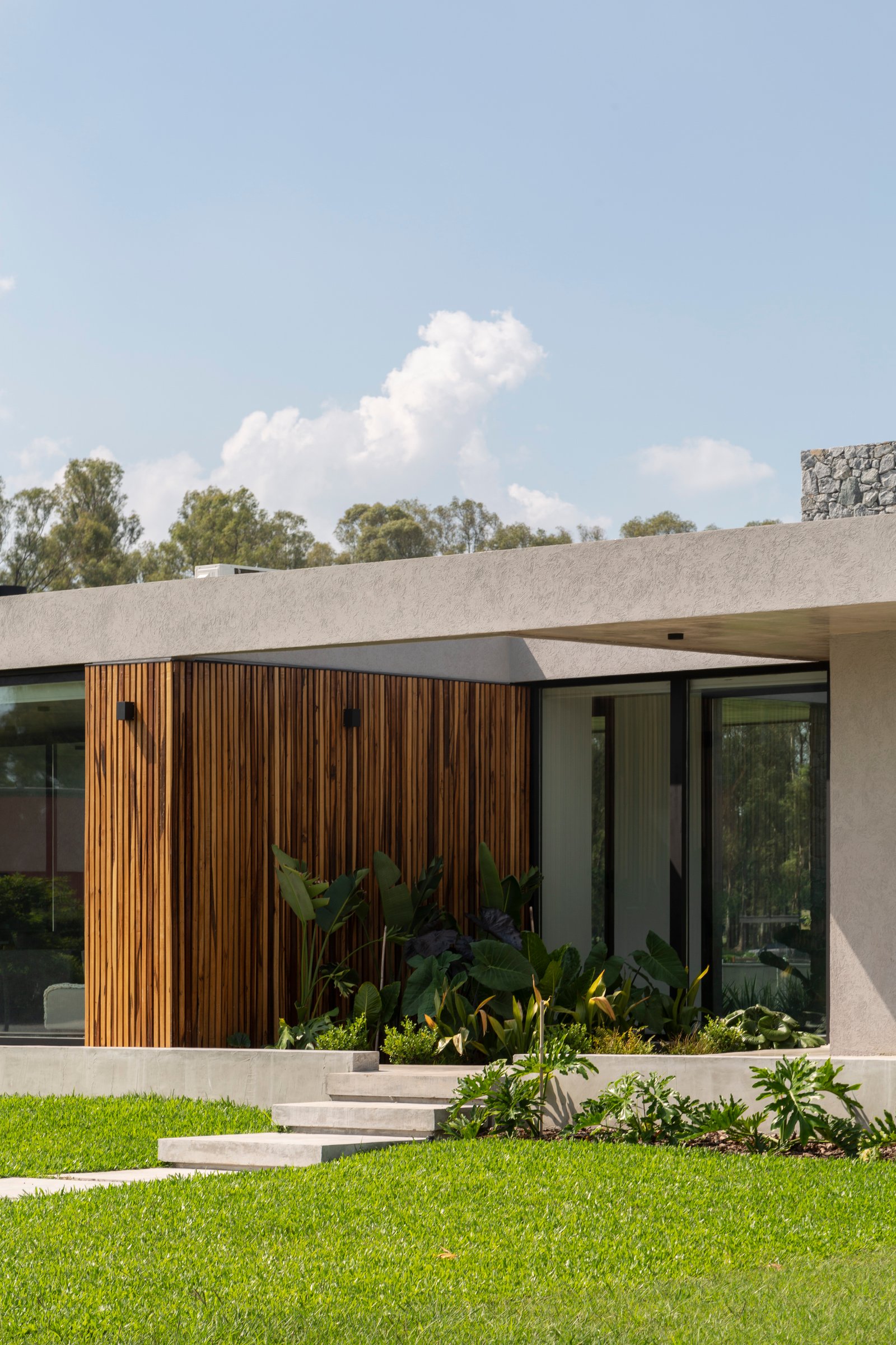 Fachada moderna con revestimiento de madera y jardín exuberante — proyecto Casa Cruz , por Grupo CRBN, en B2812 Exaltación de la Cruz