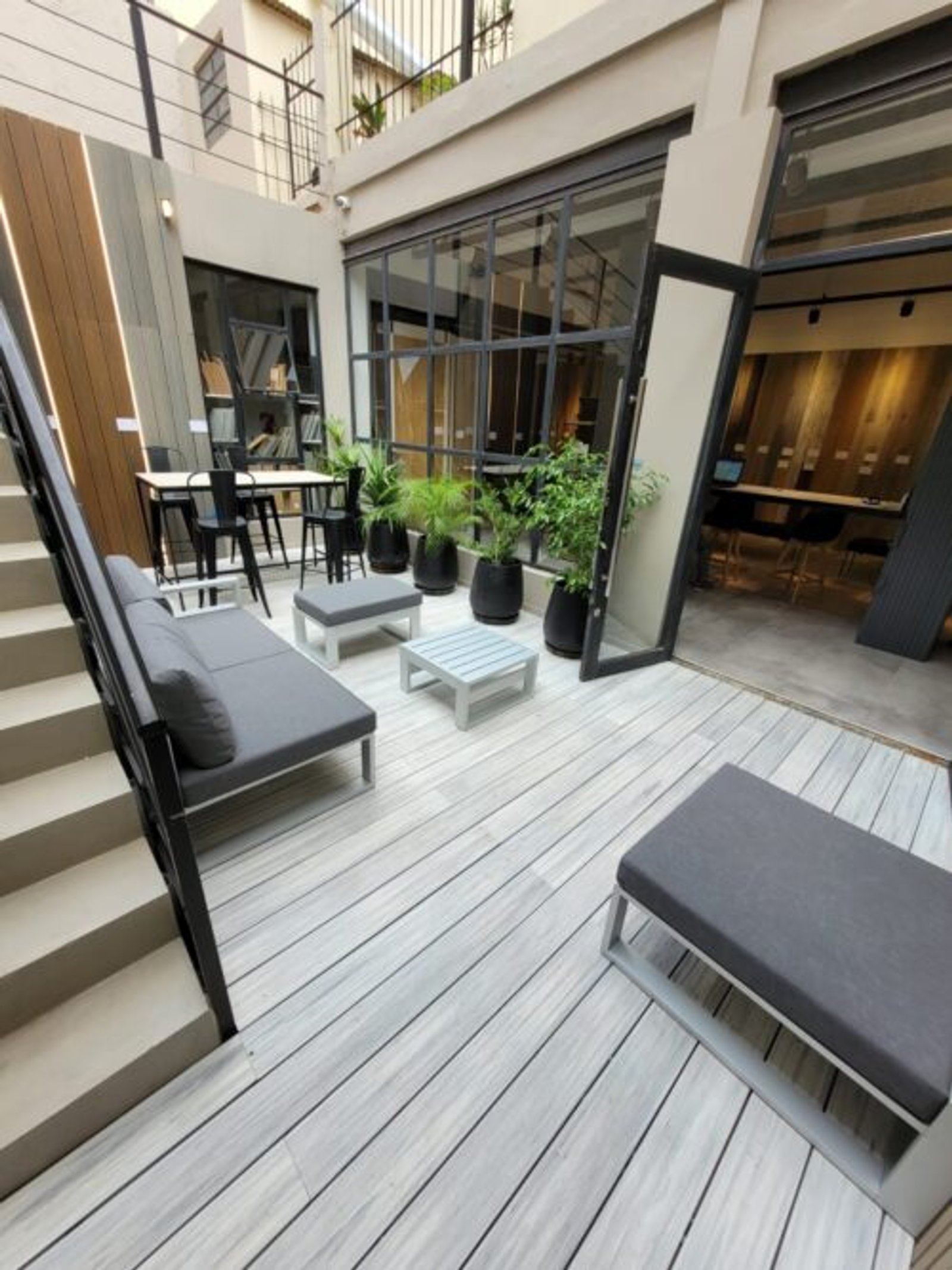 Pátio comercial moderno com deck de madeira e sofá modular cinza — projeto Outdoor, por The Flooring Company