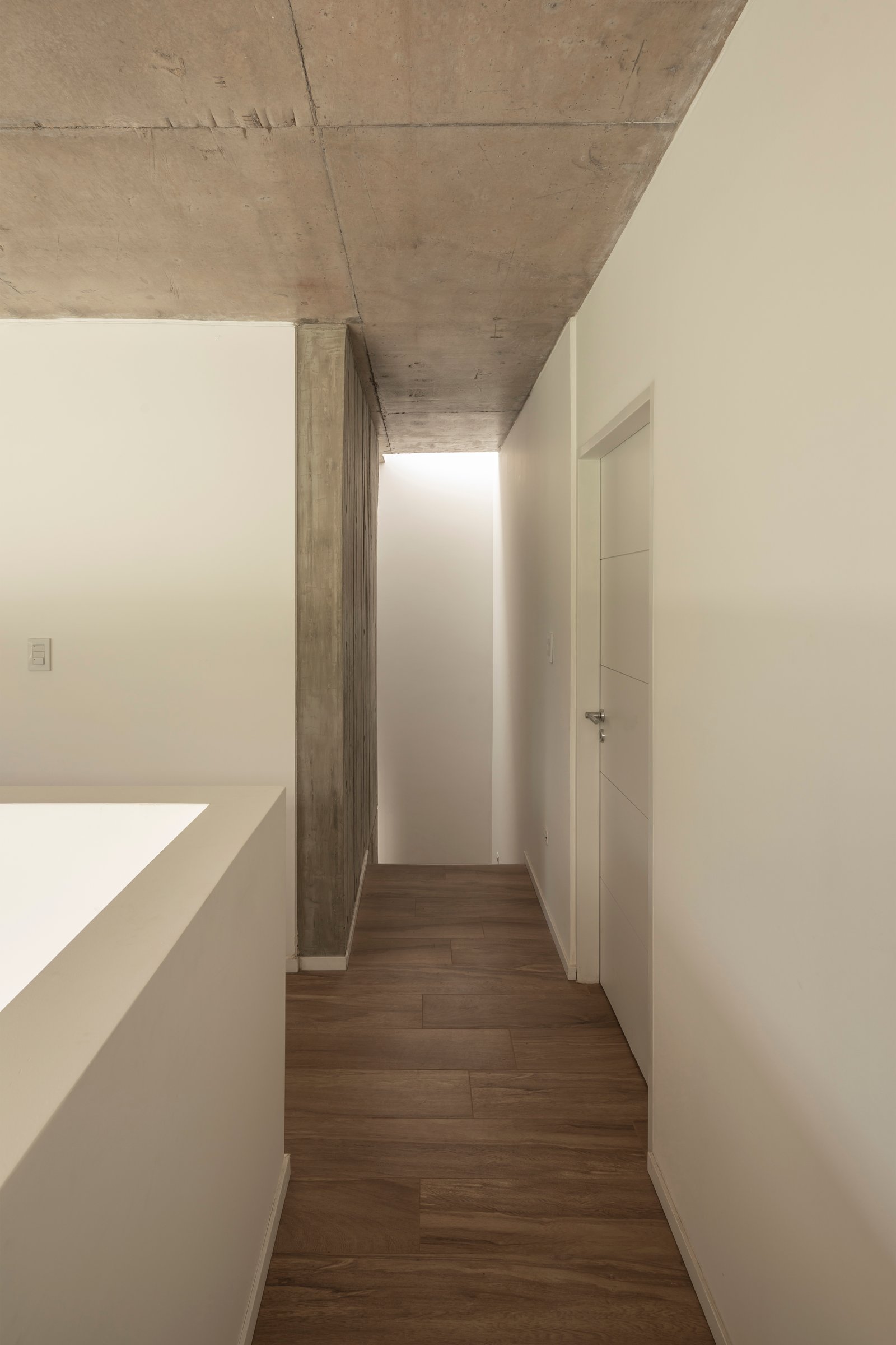 Pasillo moderno con techo de hormigón expuesto y piso de madera — proyecto Casa Emilia, por Grupo CRBN, en Parque Leloir