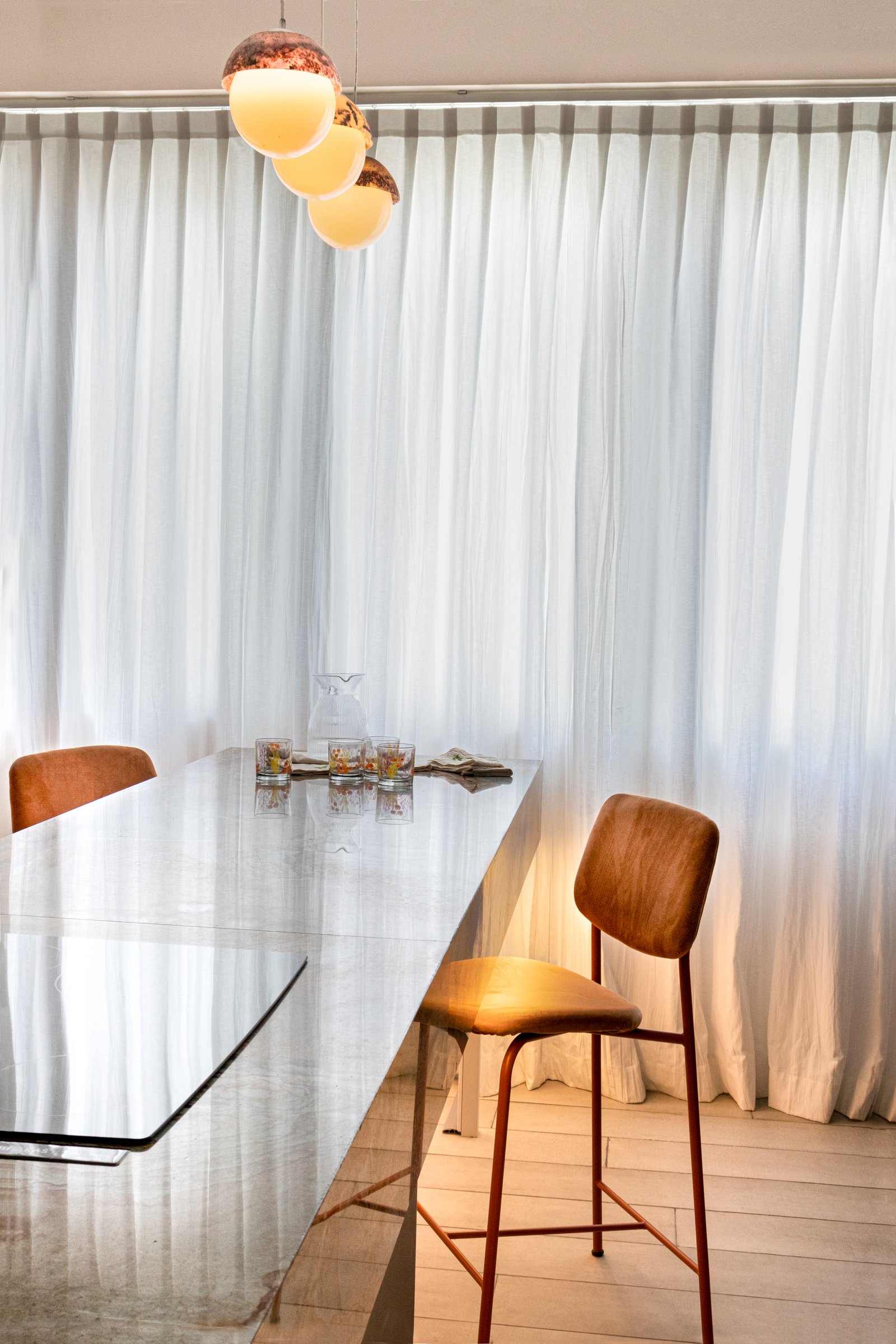 Sala de jantar moderna com mesa de metal, cadeiras de madeira, luz pendente âmbar — projeto Flor de mar azul, por KUPERDESIGN CONSTRUCCIONES SRL, em Cdad. Autónoma de Buenos Aires