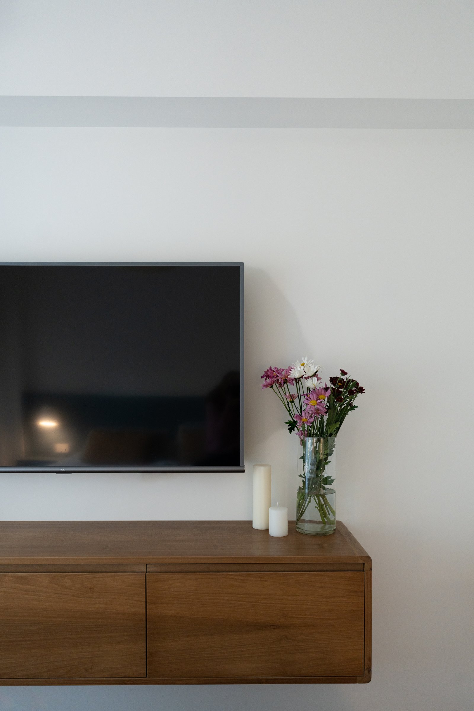 Sala de estar moderna com móvel flutuante de madeira e TV em parede branca — projeto Ugarte, por Estudio BDM, em Cdad. Autónoma de Buenos Aires