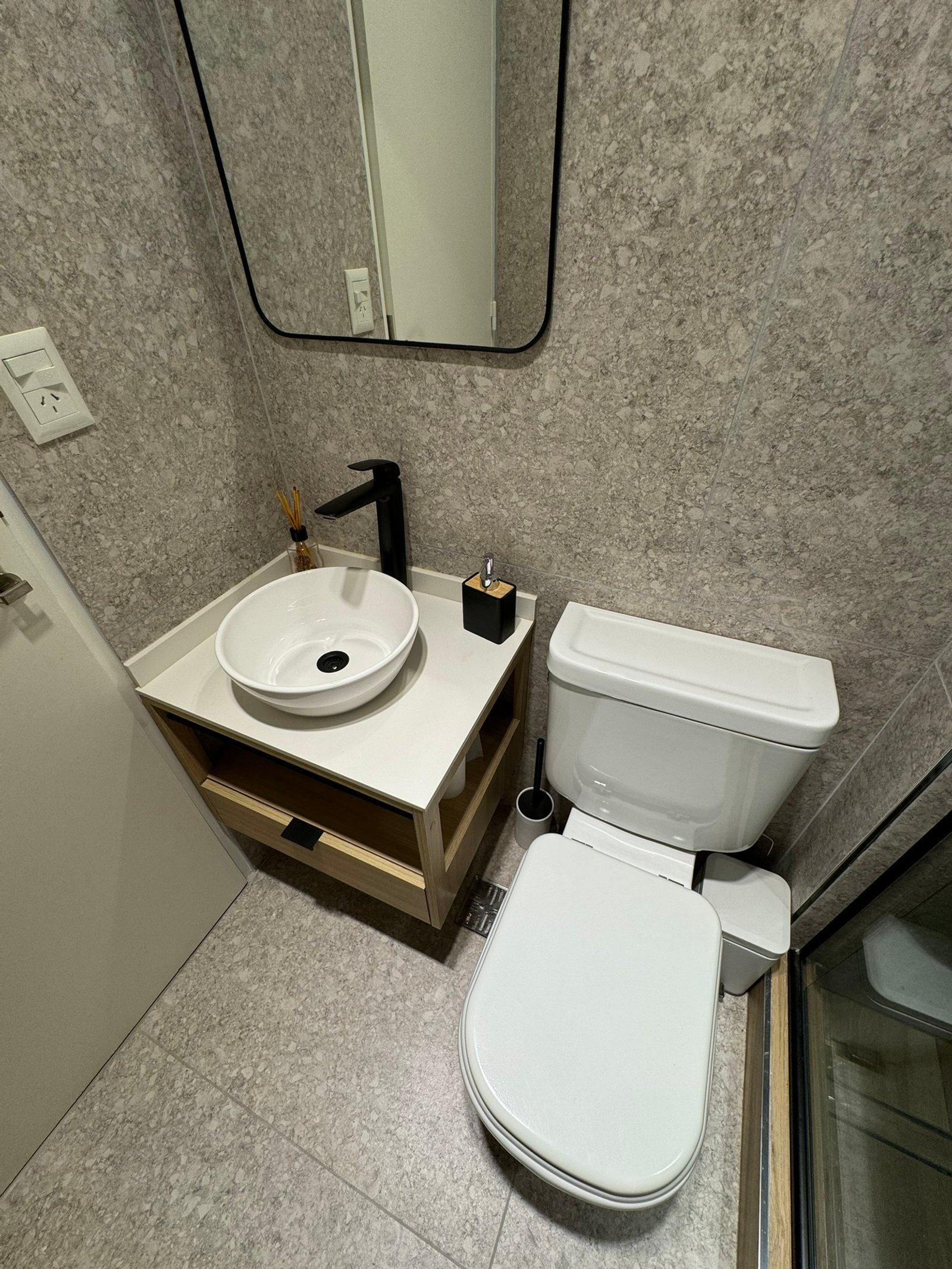 Baño moderno con paredes de piedra, mueble flotante y grifería negra — proyecto Salguero II, por MDBK Arquitectura, en Palermo