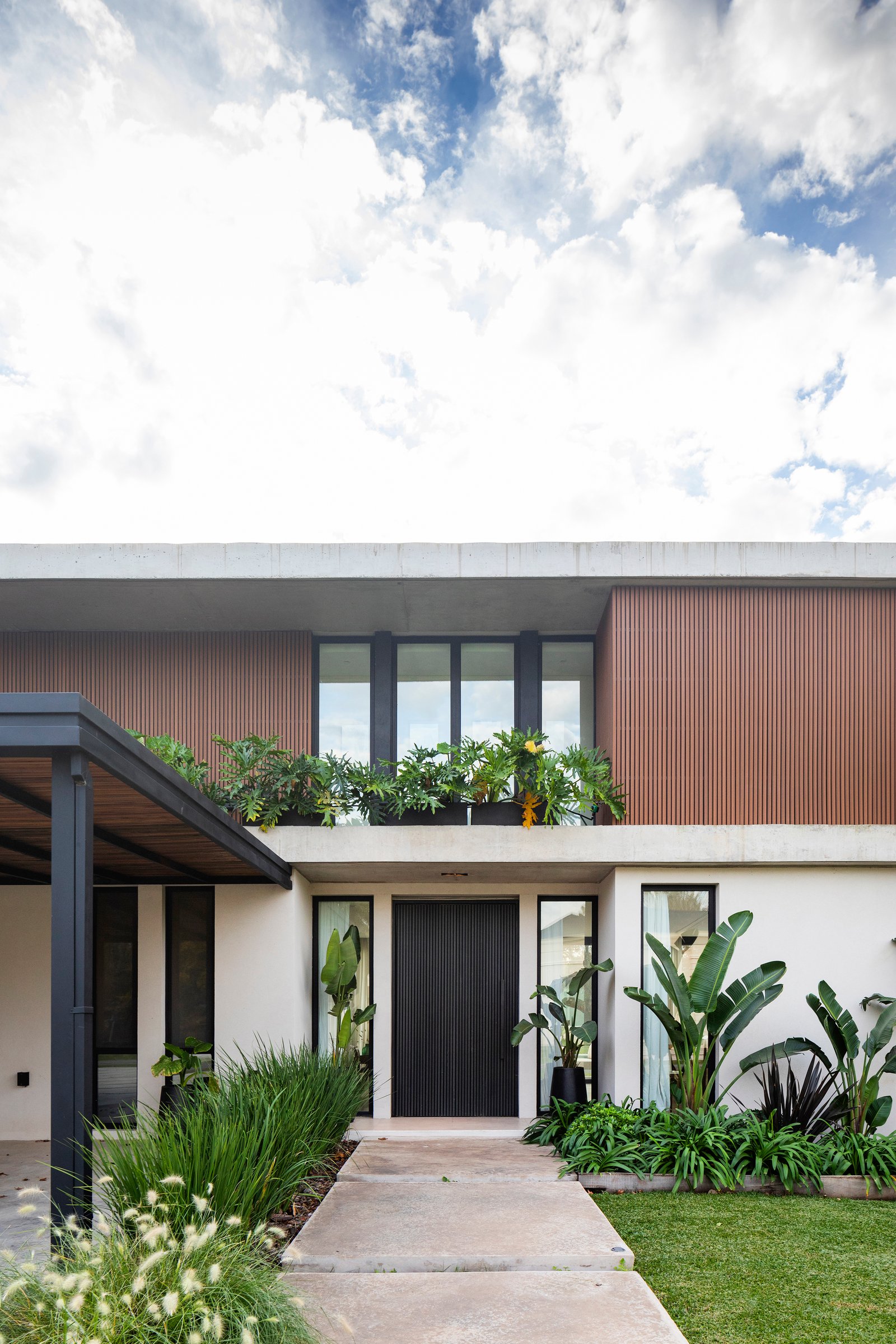 Fachada moderna com revestimento de madeira vertical e entrada com vegetação exuberante — projeto CASA HS143, por A'PRIMA - Arquitectura Sustentable, em km 7.5 Ruta 25