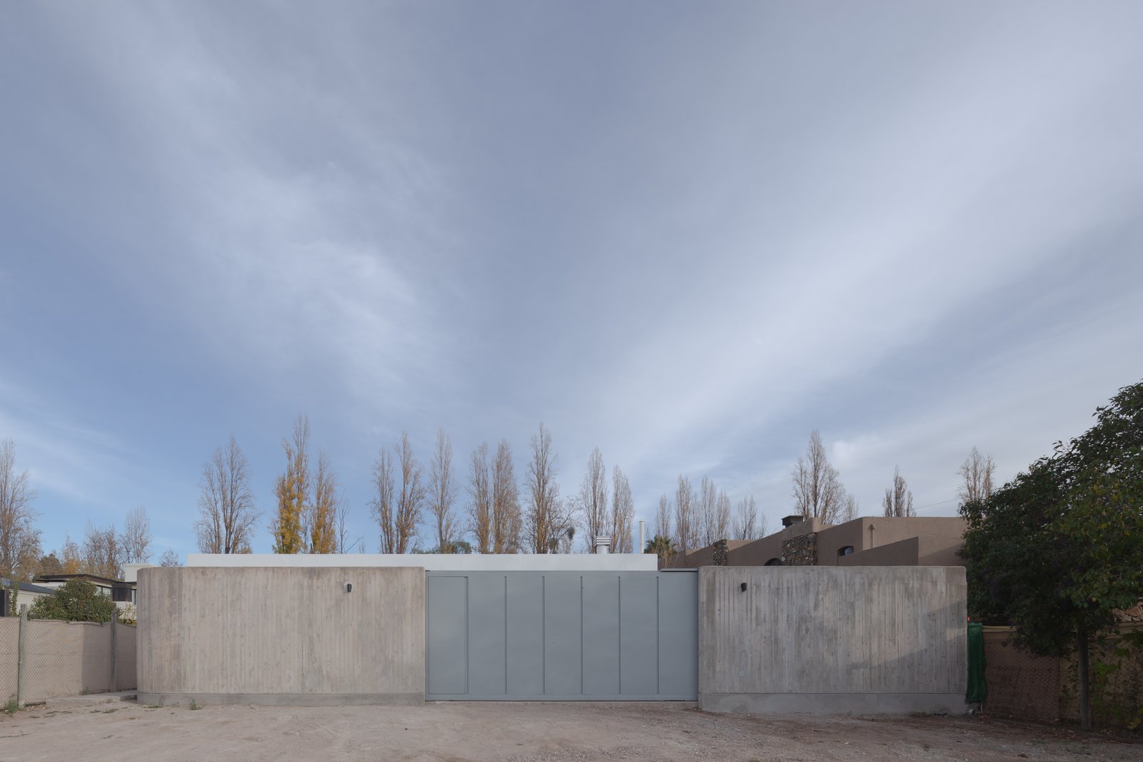 fachada moderna de hormigón con portón metálico — proyecto Vivienda CCE, por ONA - Oficina Nómada de Arquitectura, en M5505 Chacras de Coria