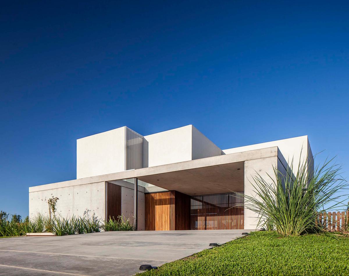 Fachada moderna de concreto branco e cinza com vegetação alta — projeto CASA J2M, por GMARQ, em Belén de Escobar