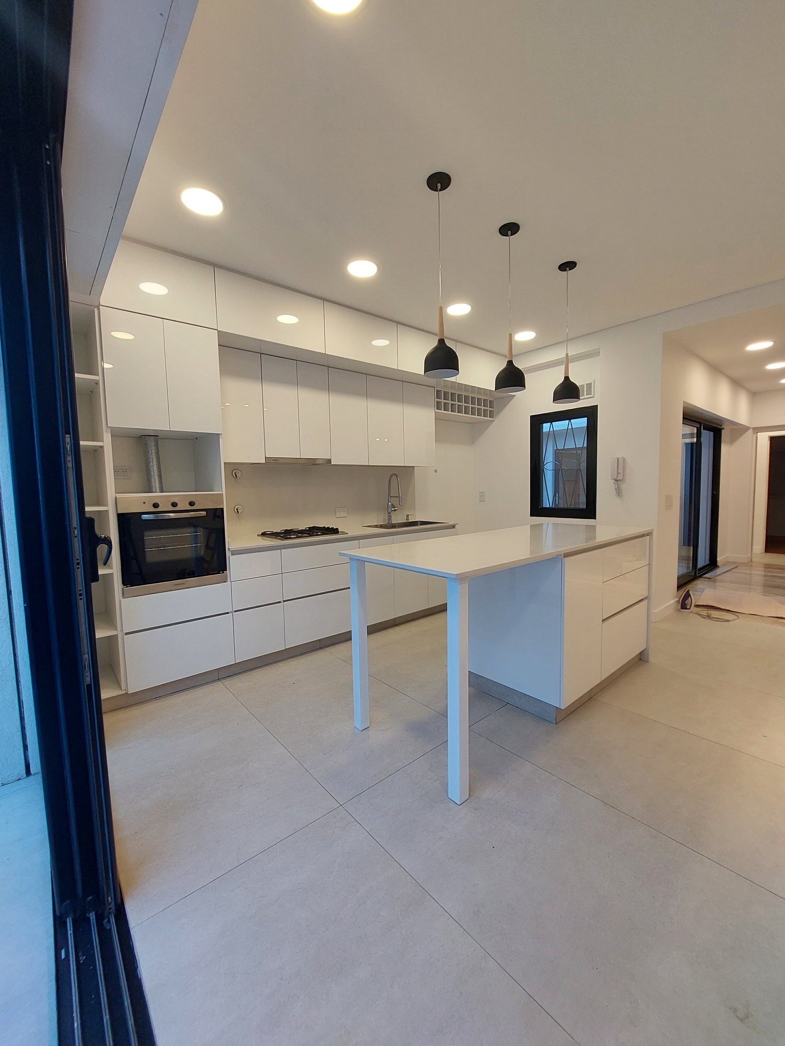 Cocina moderna de planta abierta con isla blanca y luces colgantes negras — proyecto MISTRAL, por Arquitecta, en Villa Pueyrredón