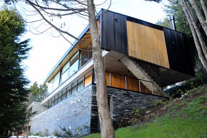 Fachada moderna en bosque con piedra y madera — proyecto Casa Península San Pedro, por Servente Larrazabal Arq, en Bariloche