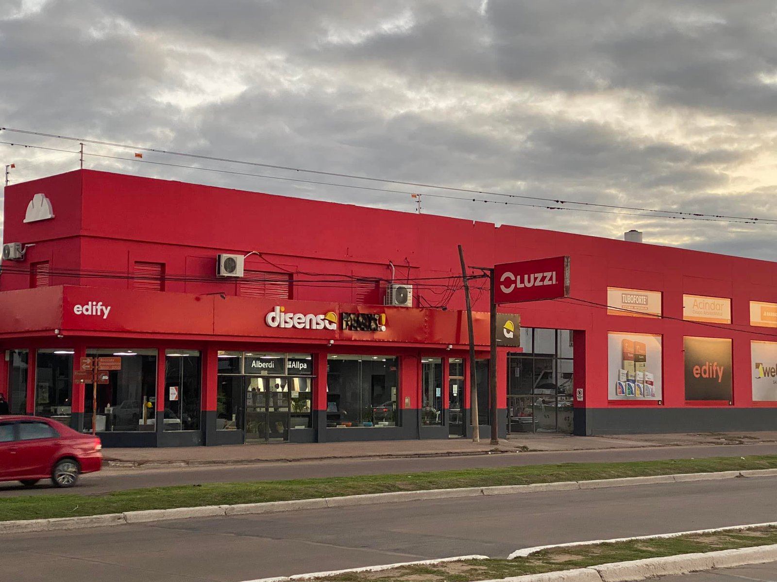 Fachada comercial roja con vidrieras y carteles — proyecto Edify Casa central. Local de venta de materiales de Construccion., por Arquitecto Gustavo Maidana, en Corrientes