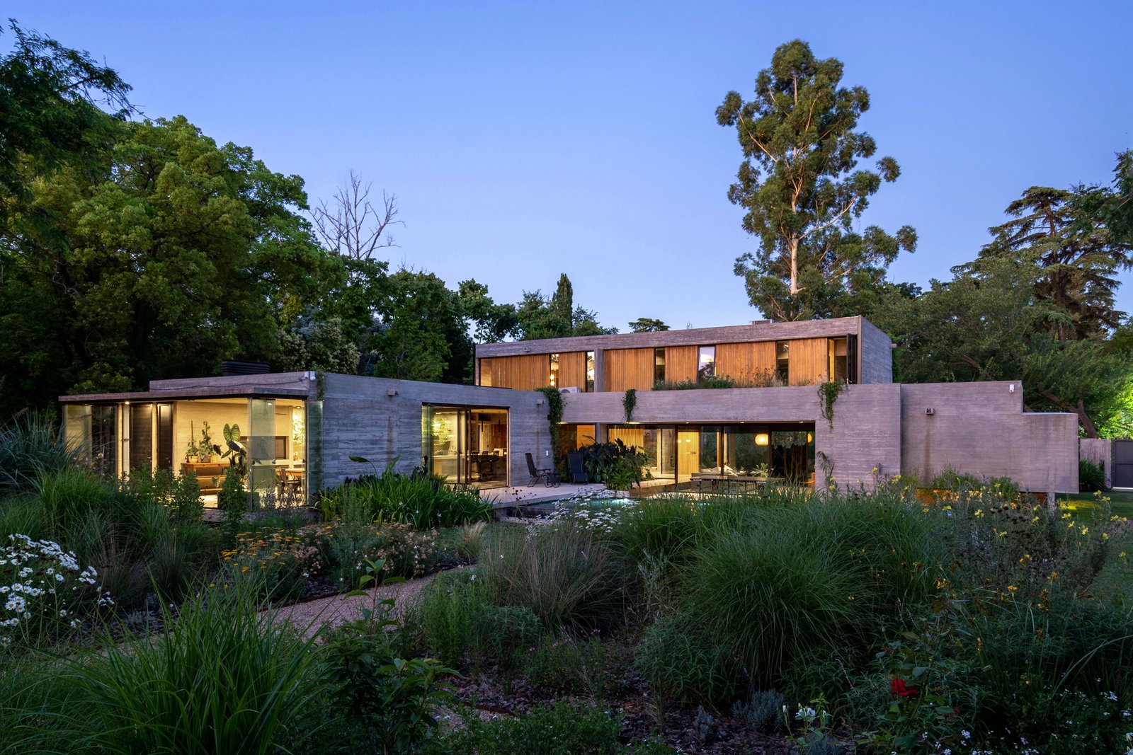 Casa moderna de hormigón y cristal con vegetación prominente — proyecto Casa Leloir, por Besonías Almeida arquitectos, en Parque Leloir