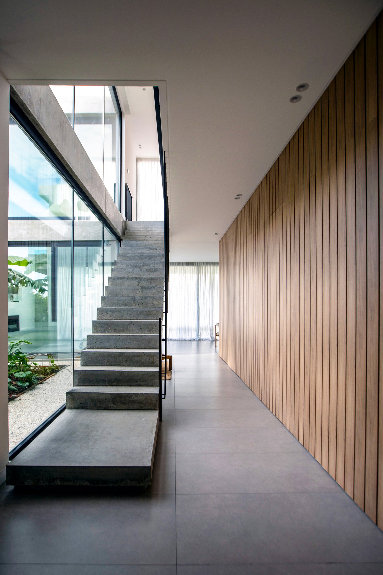 Escada de concreto, parede de ripas de madeira e janelas do chão ao teto — projeto CASA TRIBECA CONCRETE BROADWAY, por ILVA, em Provincia de Buenos Aires