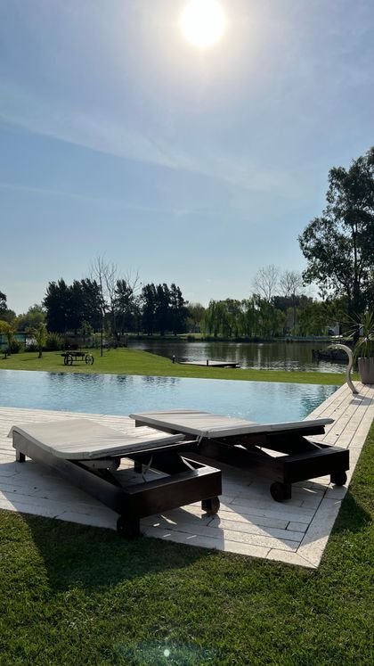 Pileta con deck de madera y tumbonas en parque junto al río — proyecto Casa Chacras, por RY Construir Estudio, en San Vicente