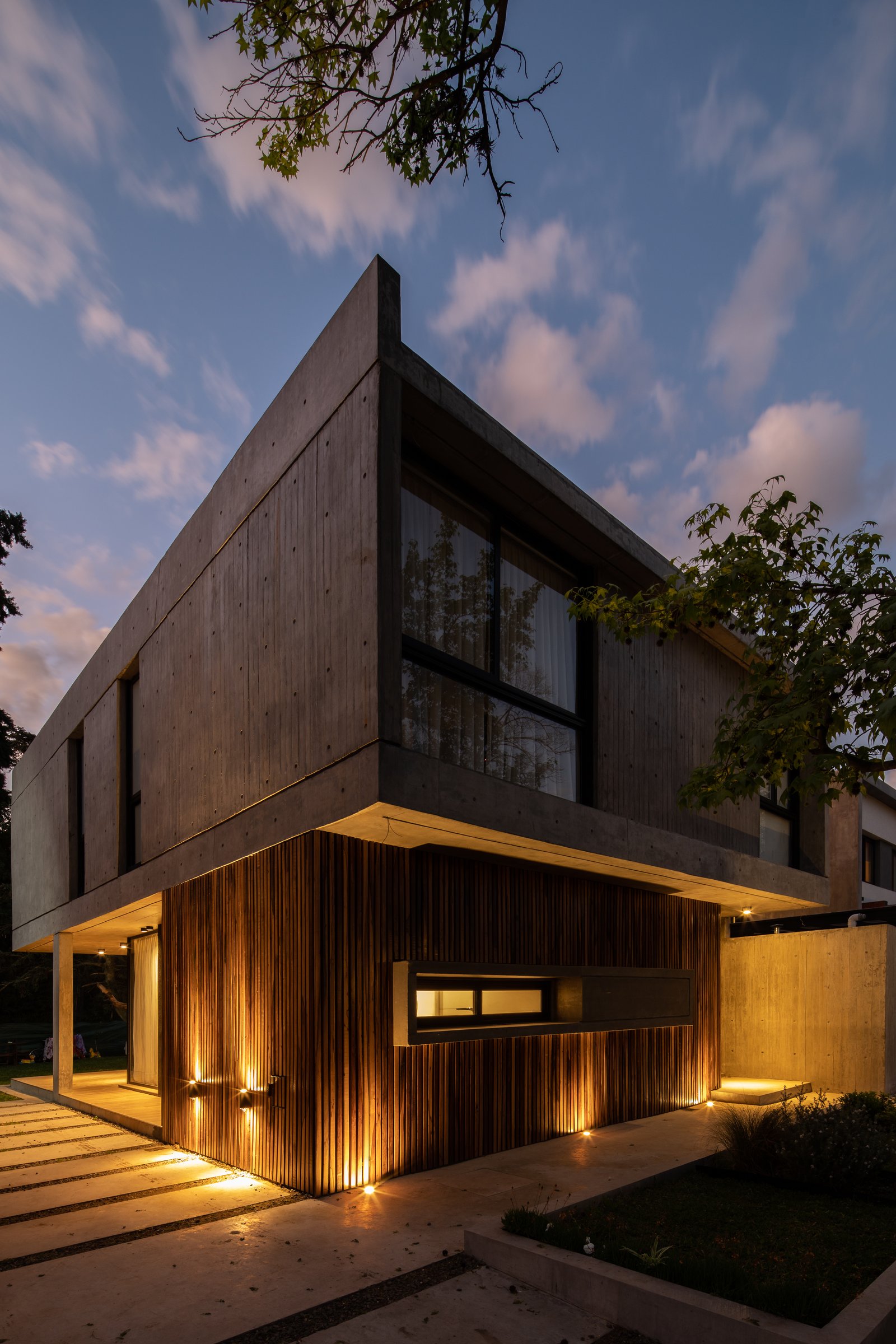 fachada moderna de hormigón y madera con luz nocturna — proyecto Casa Emilia, por Grupo CRBN, en Parque Leloir