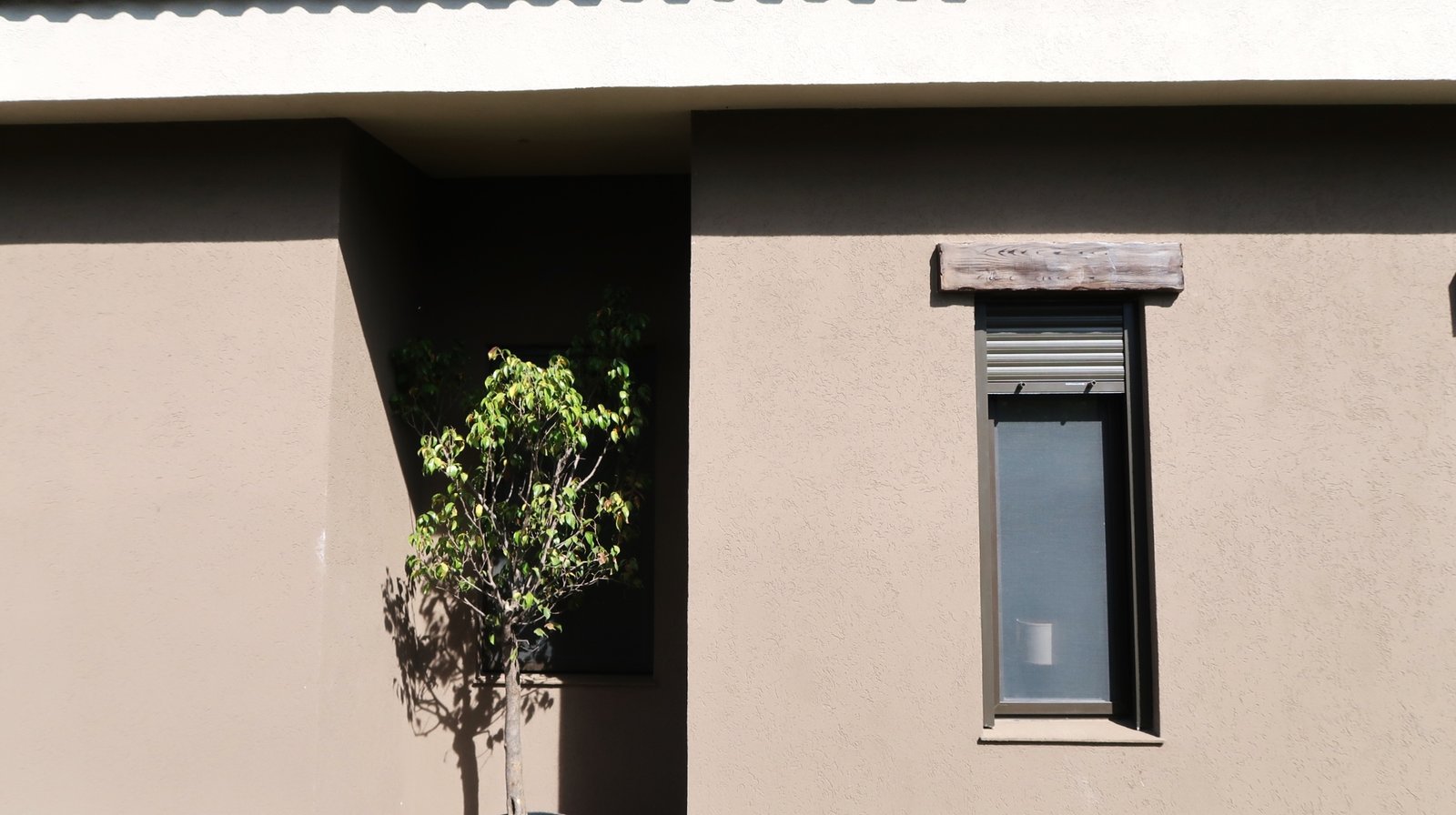 Fachada de casa moderna con estuco beige y ventana oscura — proyecto Casa La Paz, por Luciana González Anderson, en Salta