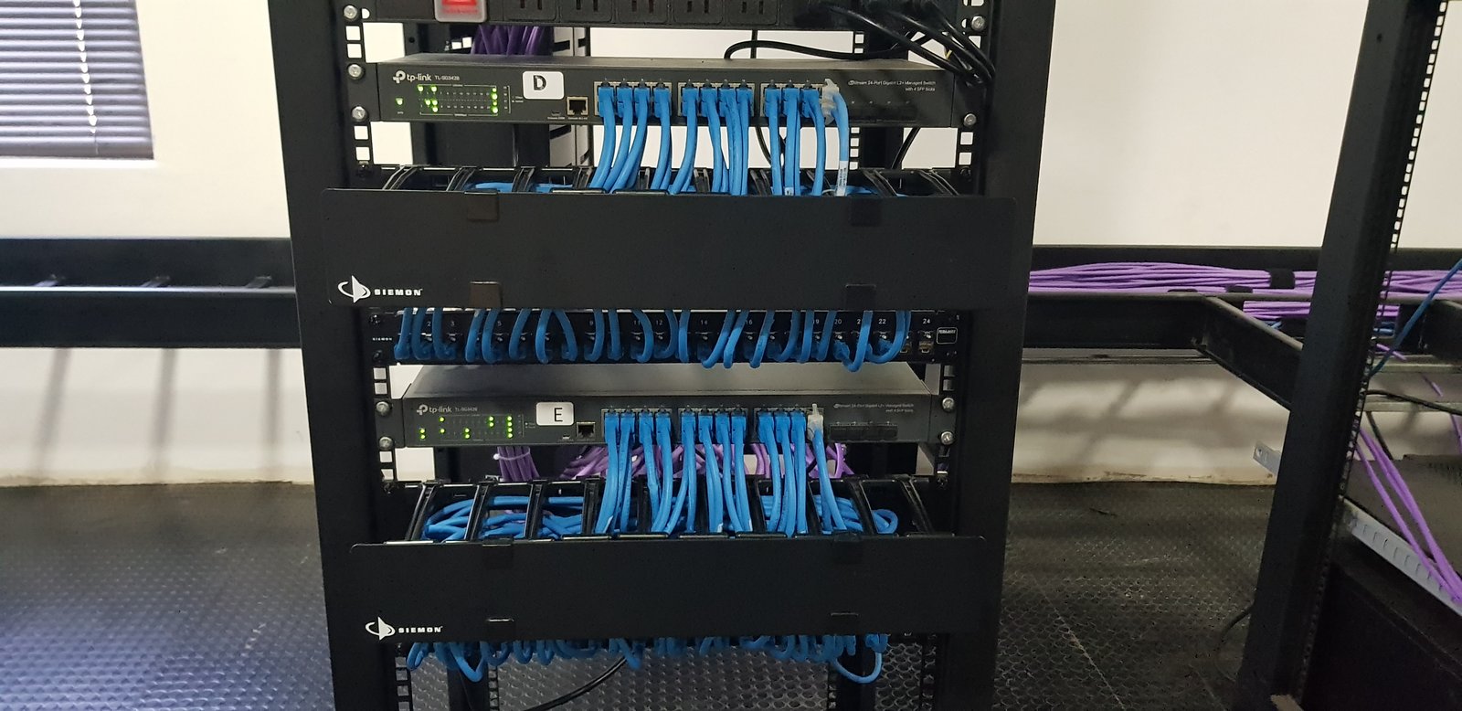 Rack de servidores con cables de red azules y púrpuras — proyecto Montajes eléctricos en oficinas Comerciales , por Mantenimientos Comerciales Leon , en Buenos Aires