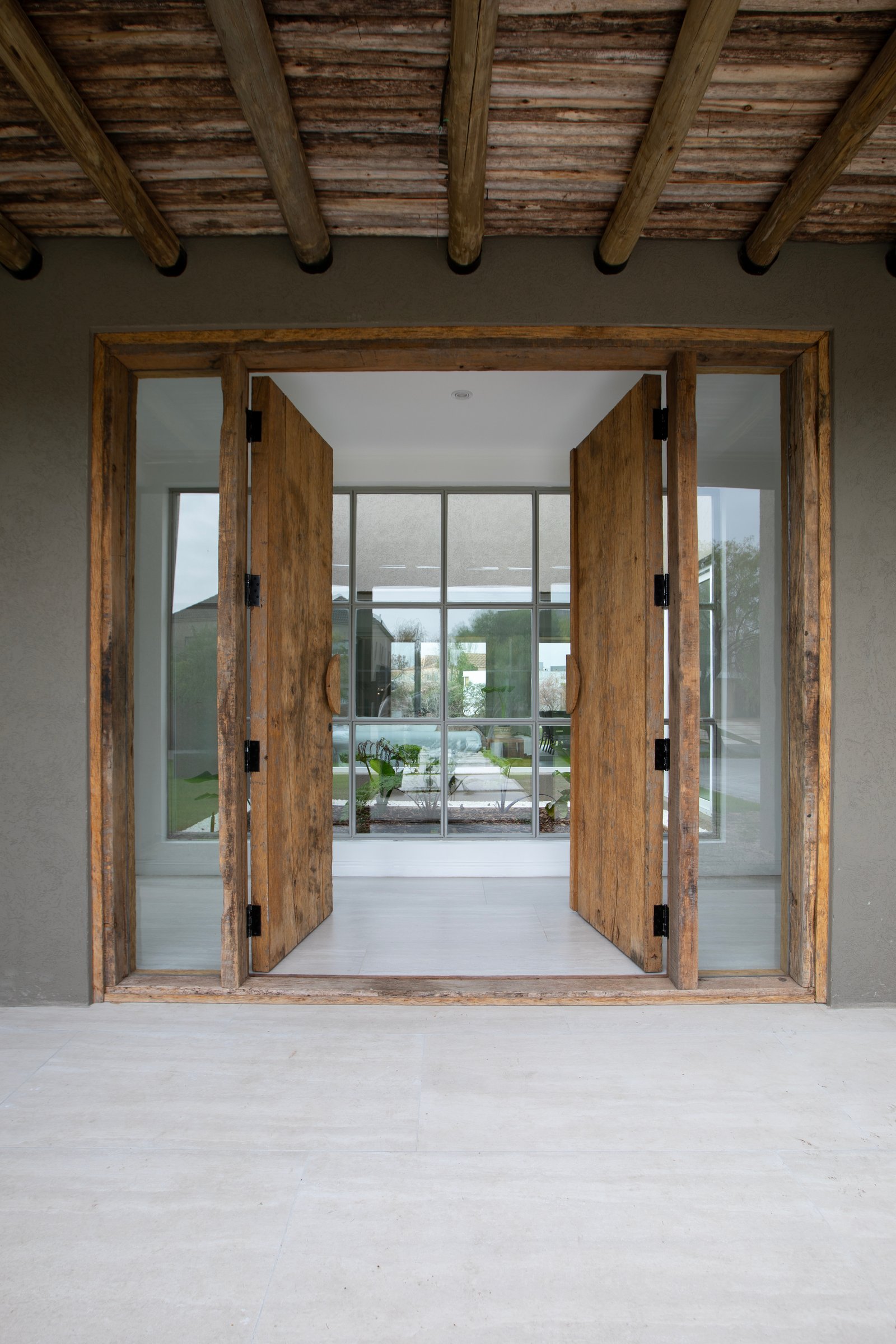 Puerta rústica doble de madera con amplios ventanales de vidrio y techo de vigas expuestas — proyecto OBRA EL RETIRO, por ILVA, en Provincia de Buenos Aires