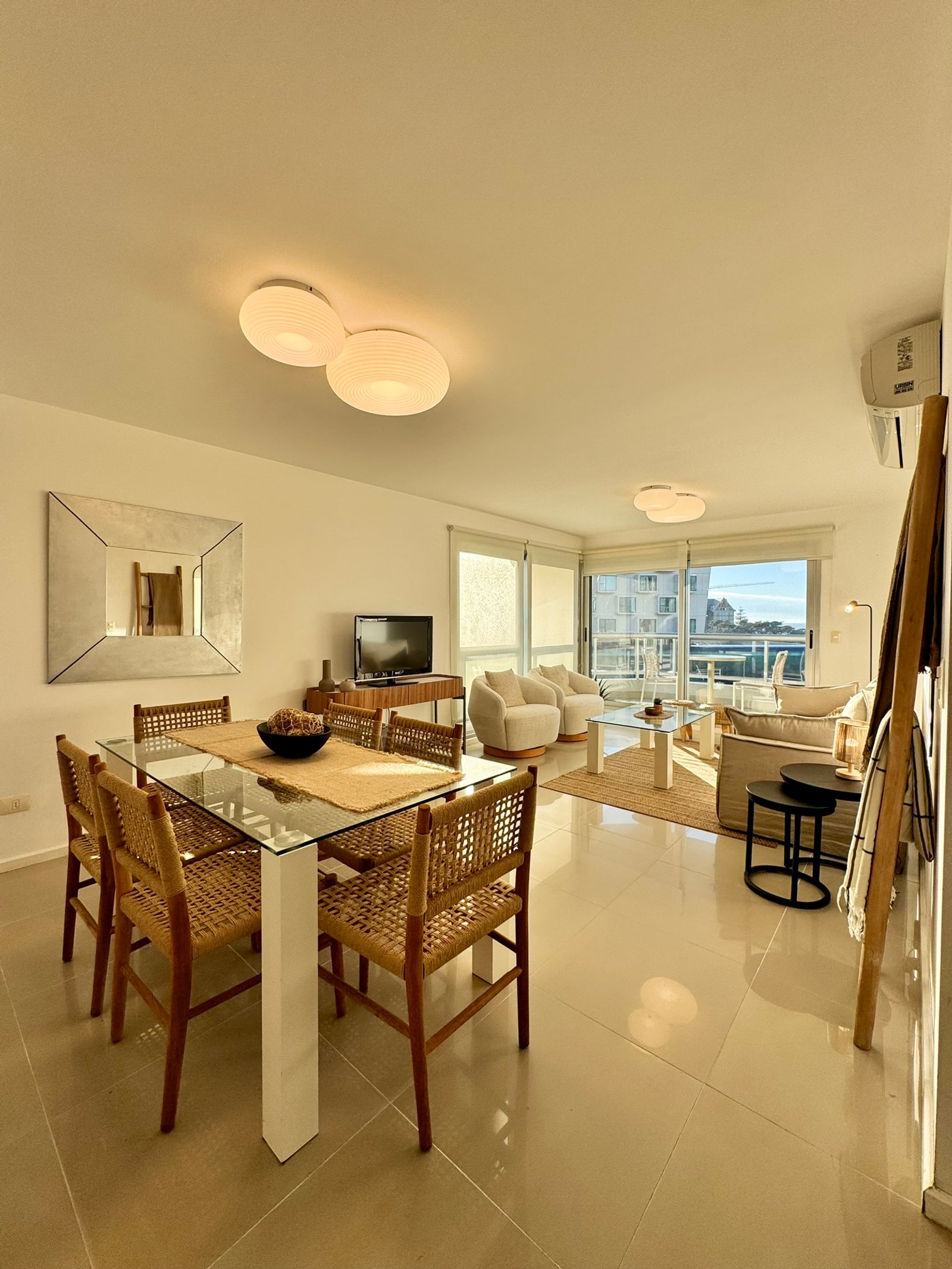 Comedor moderno con mesa de vidrio y sillas de rattan — proyecto Quartier Punta del Este, por MDBK Arquitectura, en Punta del Este