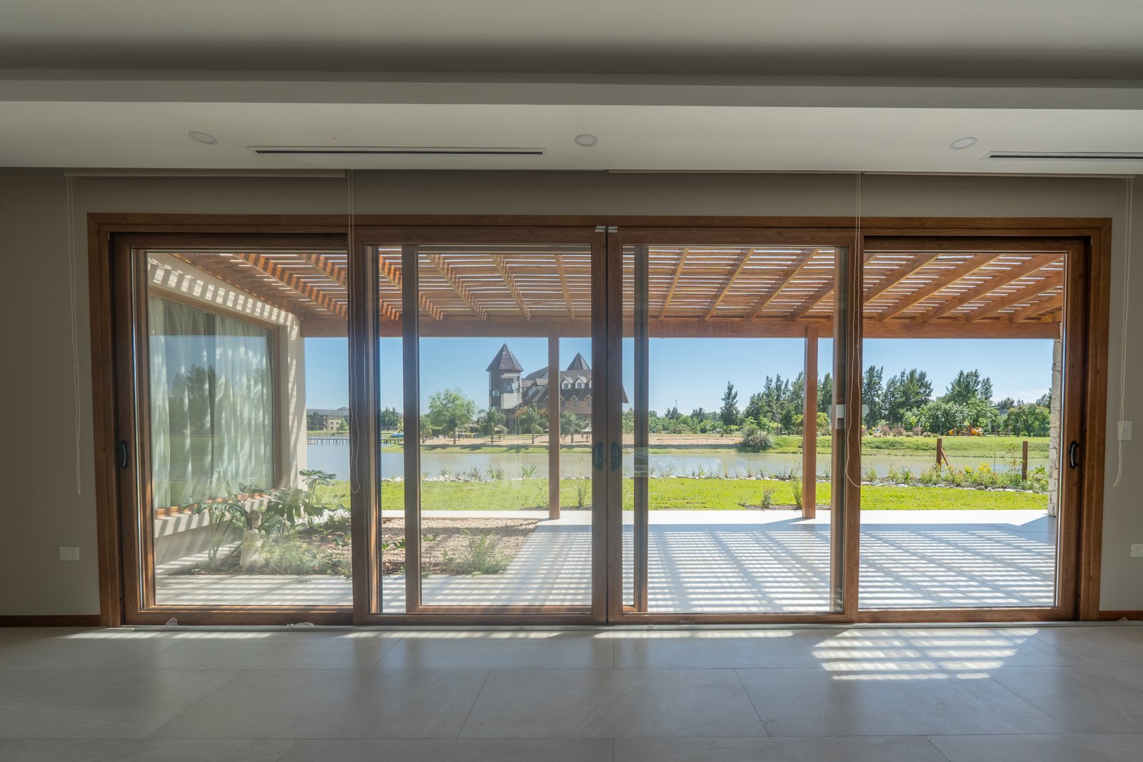 Living exterior con puertas corredizas de vidrio y vista al lago — proyecto LOTE 004, por DIKKA Arquitecta , en San Vicente