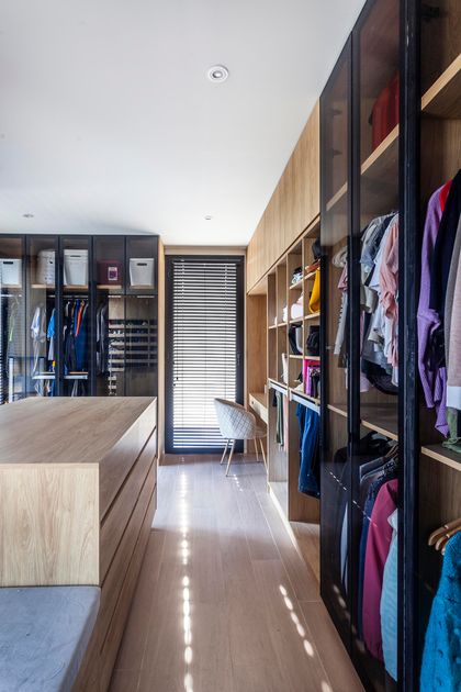Vestidor moderno con amplios estantes de madera y luz natural — proyecto CASA C313, por A'PRIMA - Arquitectura Sustentable, en Provincia de Buenos Aires