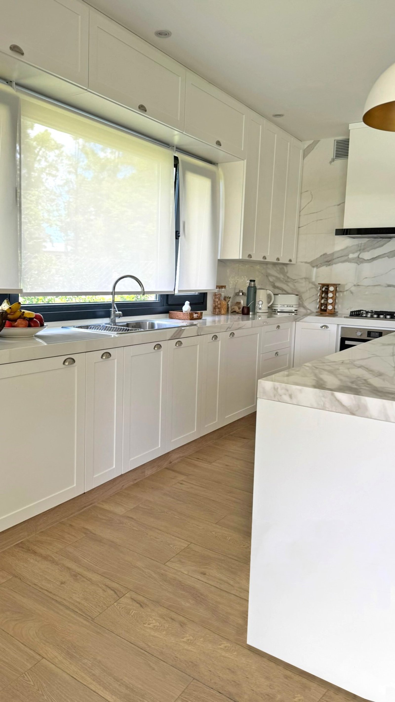 Cozinha moderna com armários brancos e bancadas de mármore, muita luz natural — projeto Casa MC, por Hermann Arquitectos, em Bv. Central