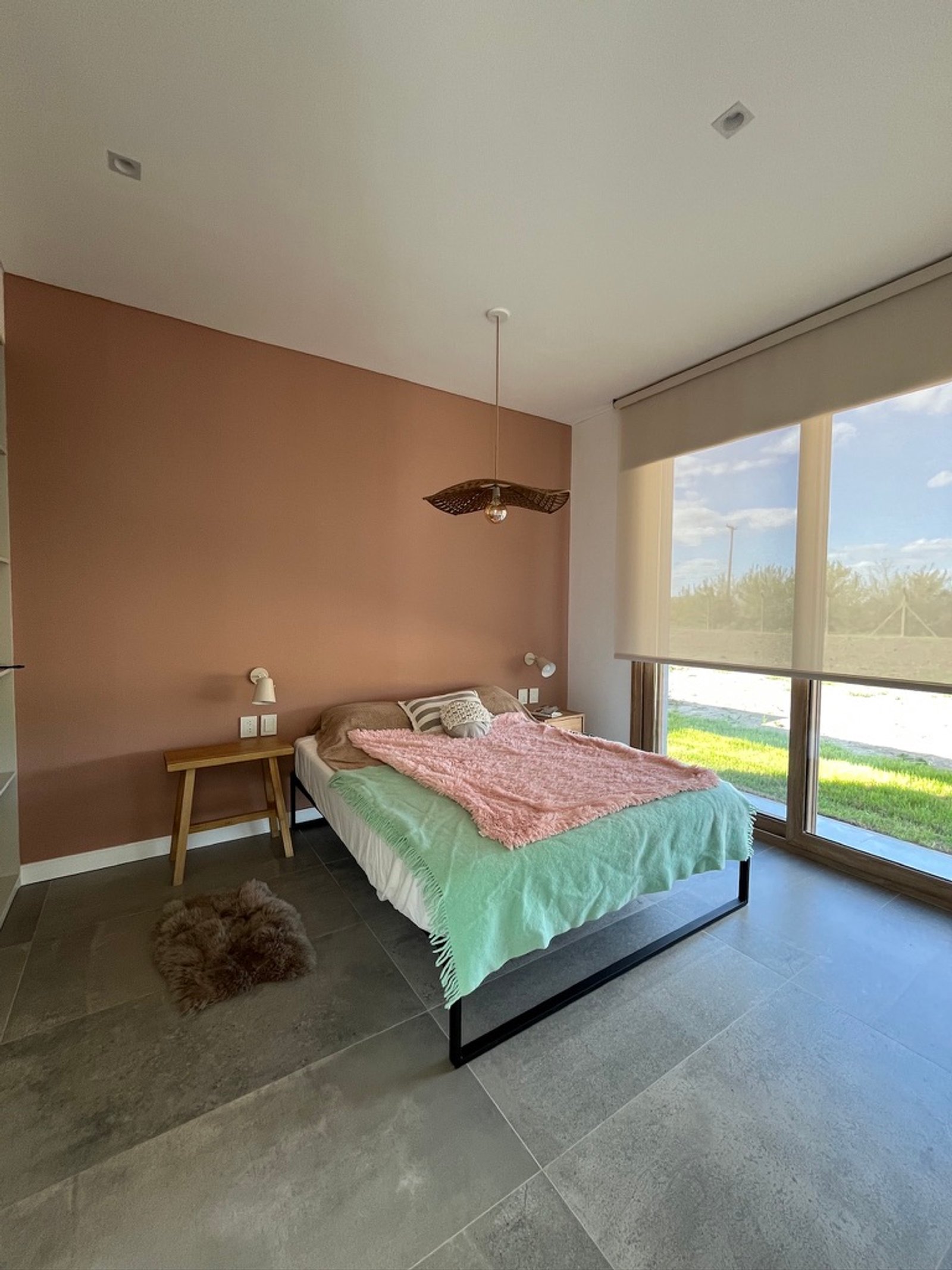 Dormitorio con pared terracota, ventana grande y luz tejida — proyecto La Colina, por Arcucci Arquitectura, en La Colina Villa de Campo