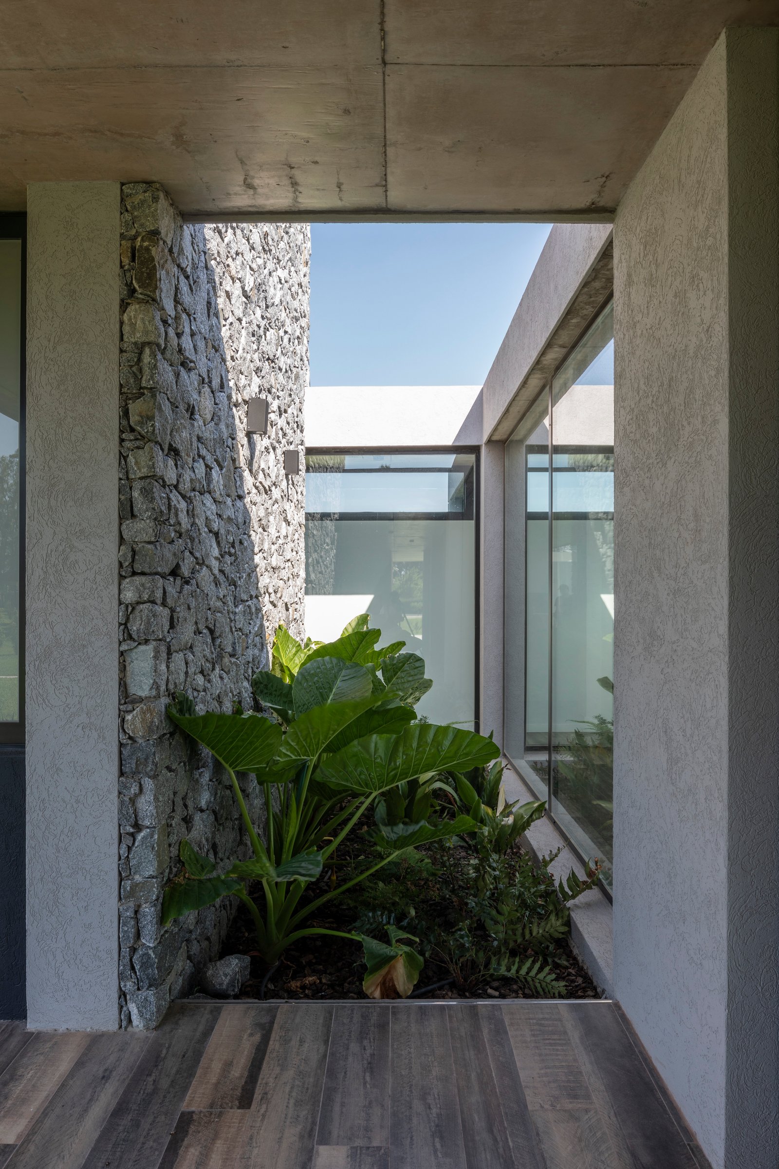 Patio moderno con muros de piedra y grandes ventanales — proyecto Casa Cruz , por Grupo CRBN, en B2812 Exaltación de la Cruz