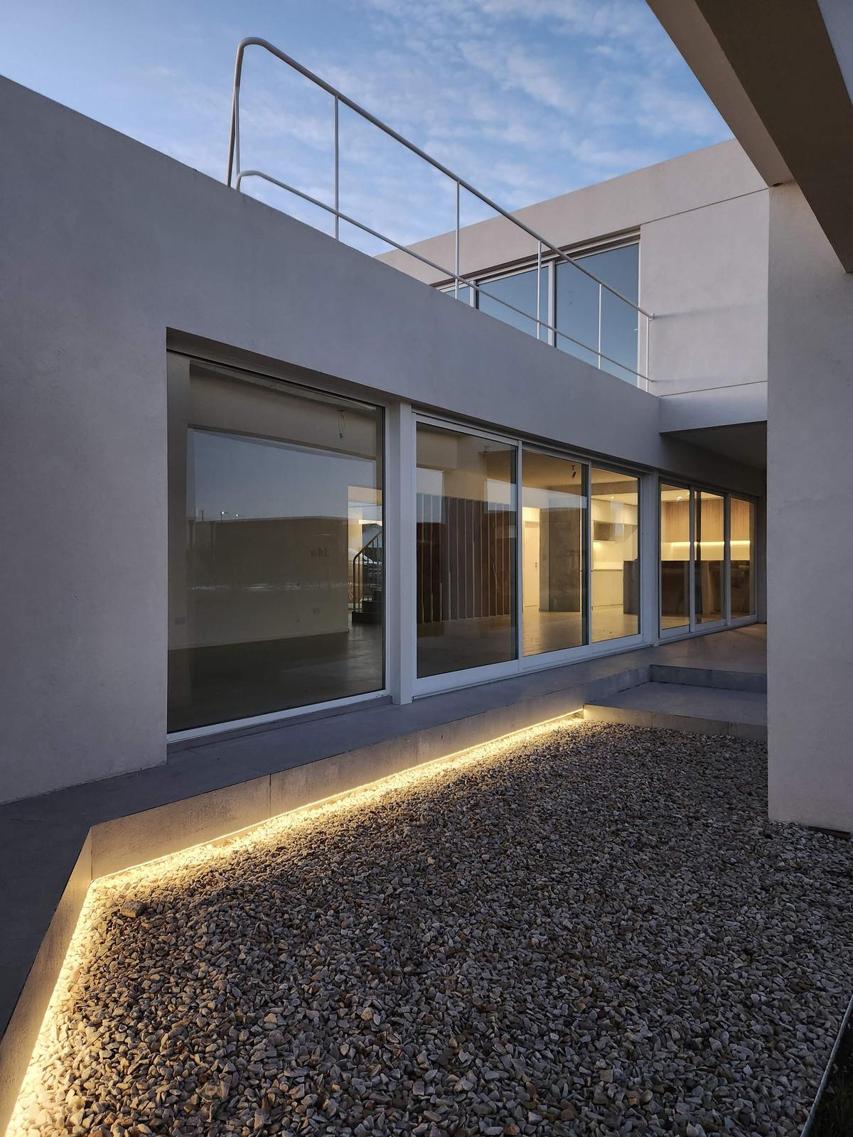 Fachada moderna brutalista com iluminação integrada e jardim de cascalho — projeto Acacias 265, por BARBALACO ARQUITECTOS, em Belén de Escobar