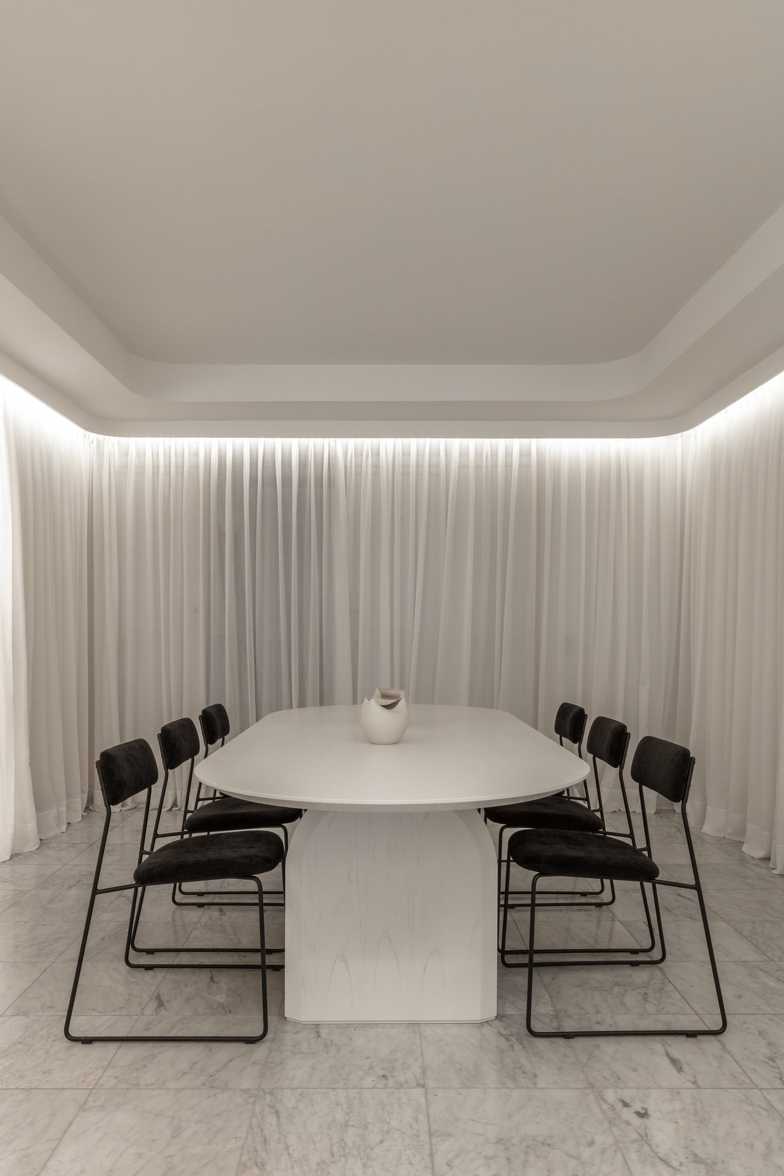 Comedor moderno con mesa ovalada blanca y sillas negras, cortinas blancas y luz indirecta — proyecto Figueroa Alcorta | Rhinoplasty meets art, por Ren Studio, en Palermo Chico