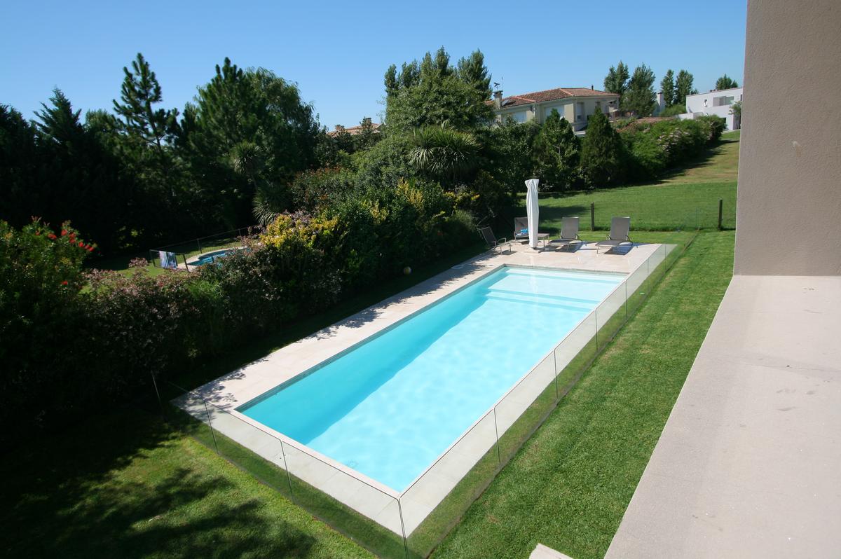 Piscina retangular moderna com deck de pedra e vegetação exuberante — projeto Inmuebles, por Geo Estudio, em Buenos Aires