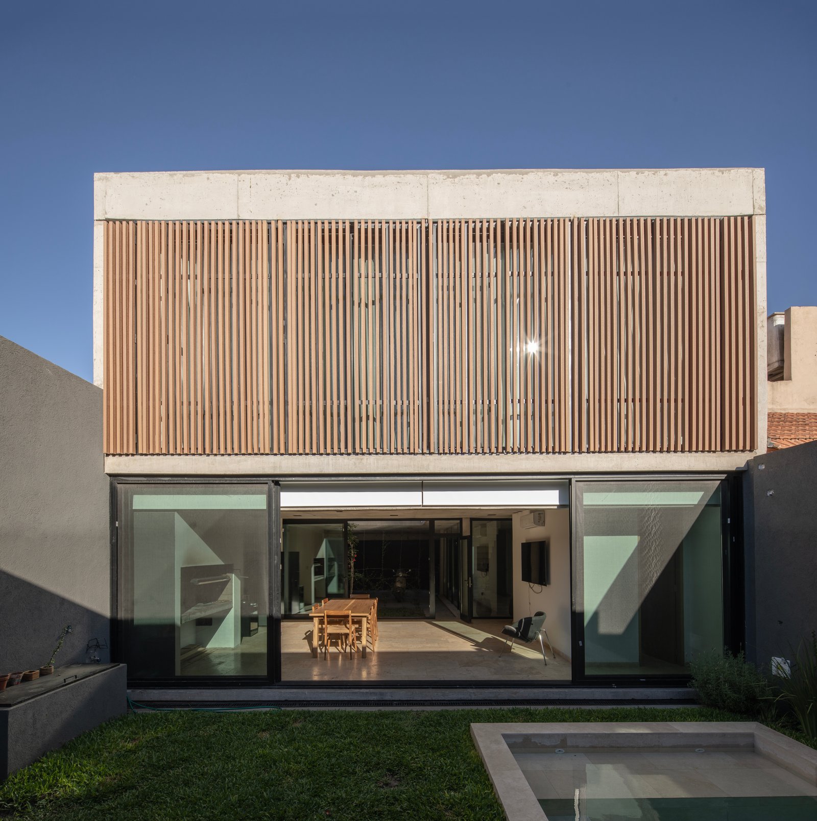 Fachada moderna con lamas de madera y amplios ventanales — proyecto Casa MECHA, por Grupo CRBN, en B1712 Castelar