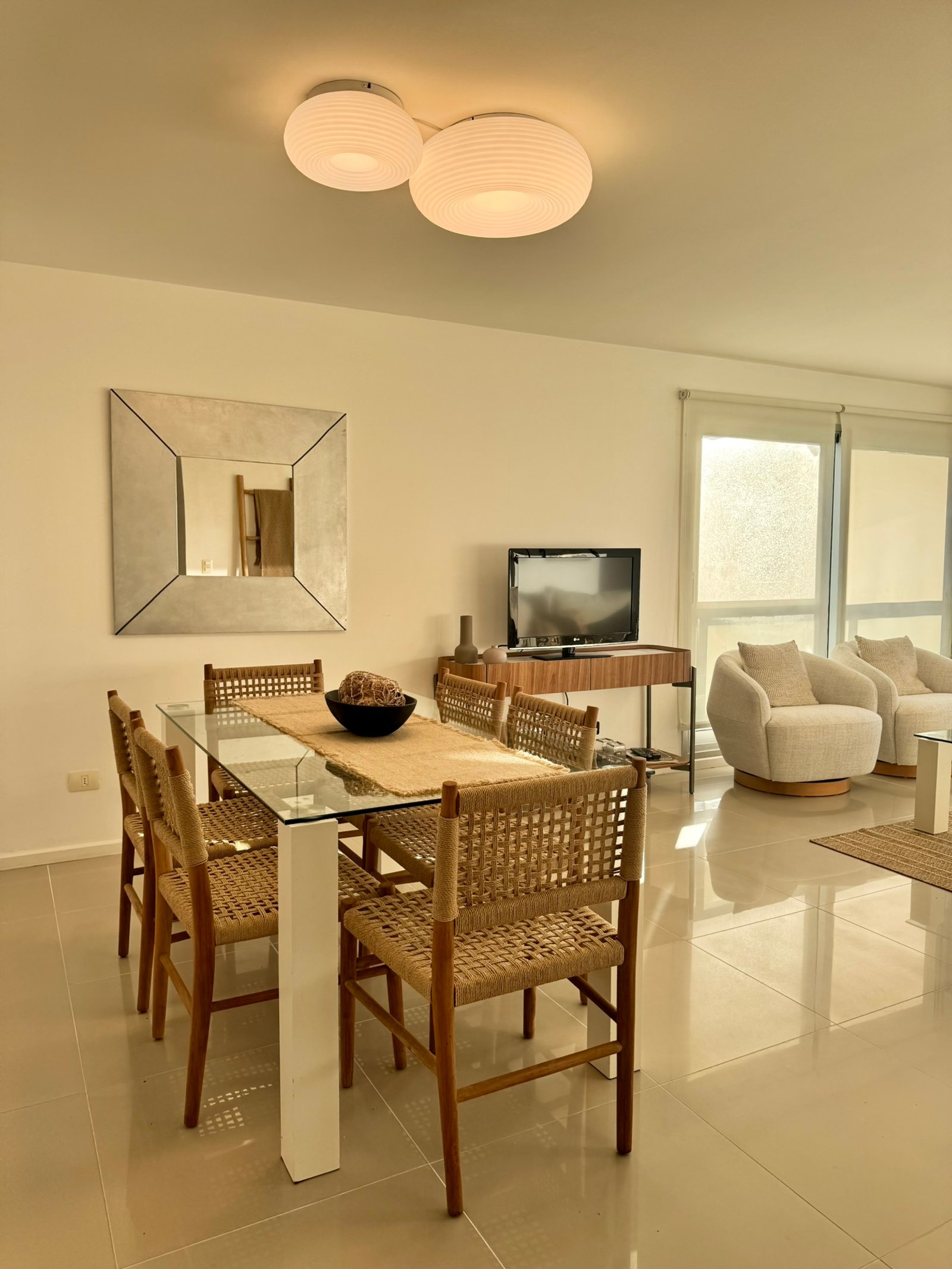 Sala de jantar moderna com mesa de vidro e cadeiras de vime — projeto Quartier Punta del Este, por MDBK Arquitectura, em Punta del Este