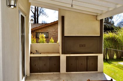 Quincho moderno con parrilla integrada y mesada de madera — proyecto Newman Benavidez, por Marconi Silva Arquitectos, en Benavidez