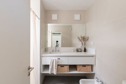 baño minimalista con mesada blanca, espejo grande y canastos de mimbre — proyecto Casa TT, por Grupo Studio, en Villa Allende