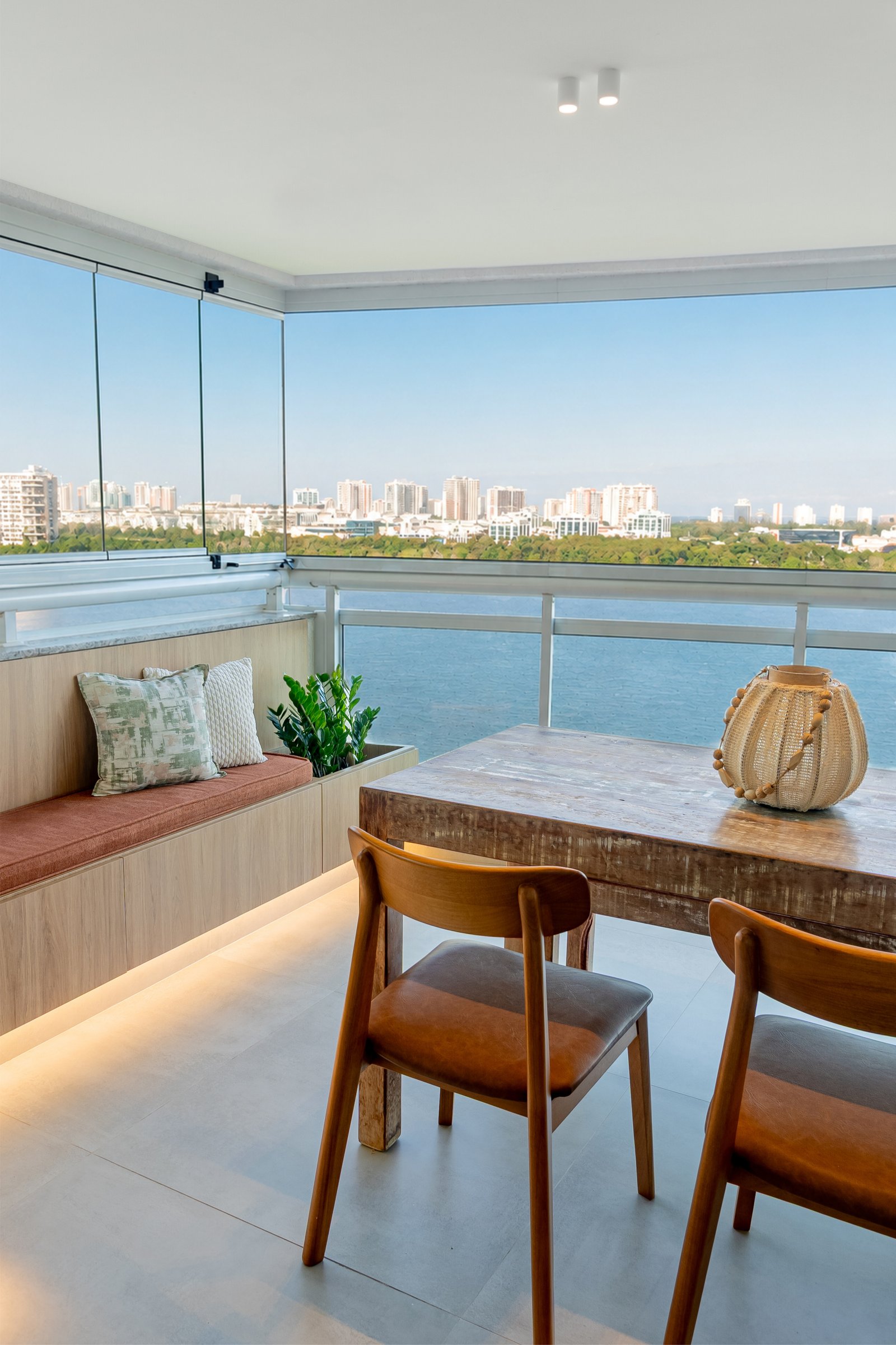 Balcón moderno con vista urbana, mesa rústica y sillas de madera — proyecto Projeto TI, por Felipe Rohen, en Rio de Janeiro