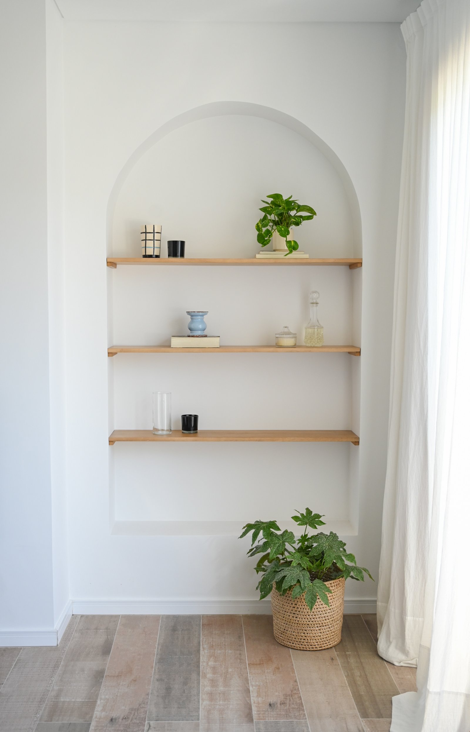 Nicho arqueado con estanterías flotantes y planta en maceta de ratán — proyecto Living, por CASA1-TROMEN, en Bella Vista