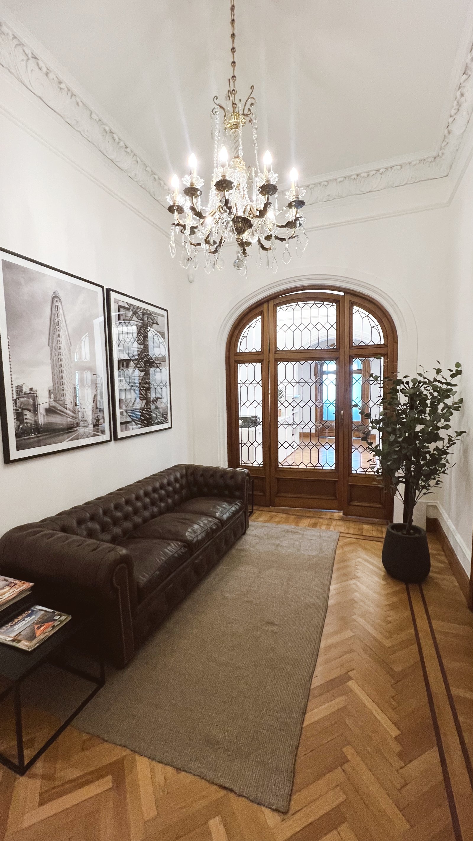 Sofá de couro marrom em recepção com lustre de cristal — projeto MONTEVIDEO, por Estudio RG, em Recoleta