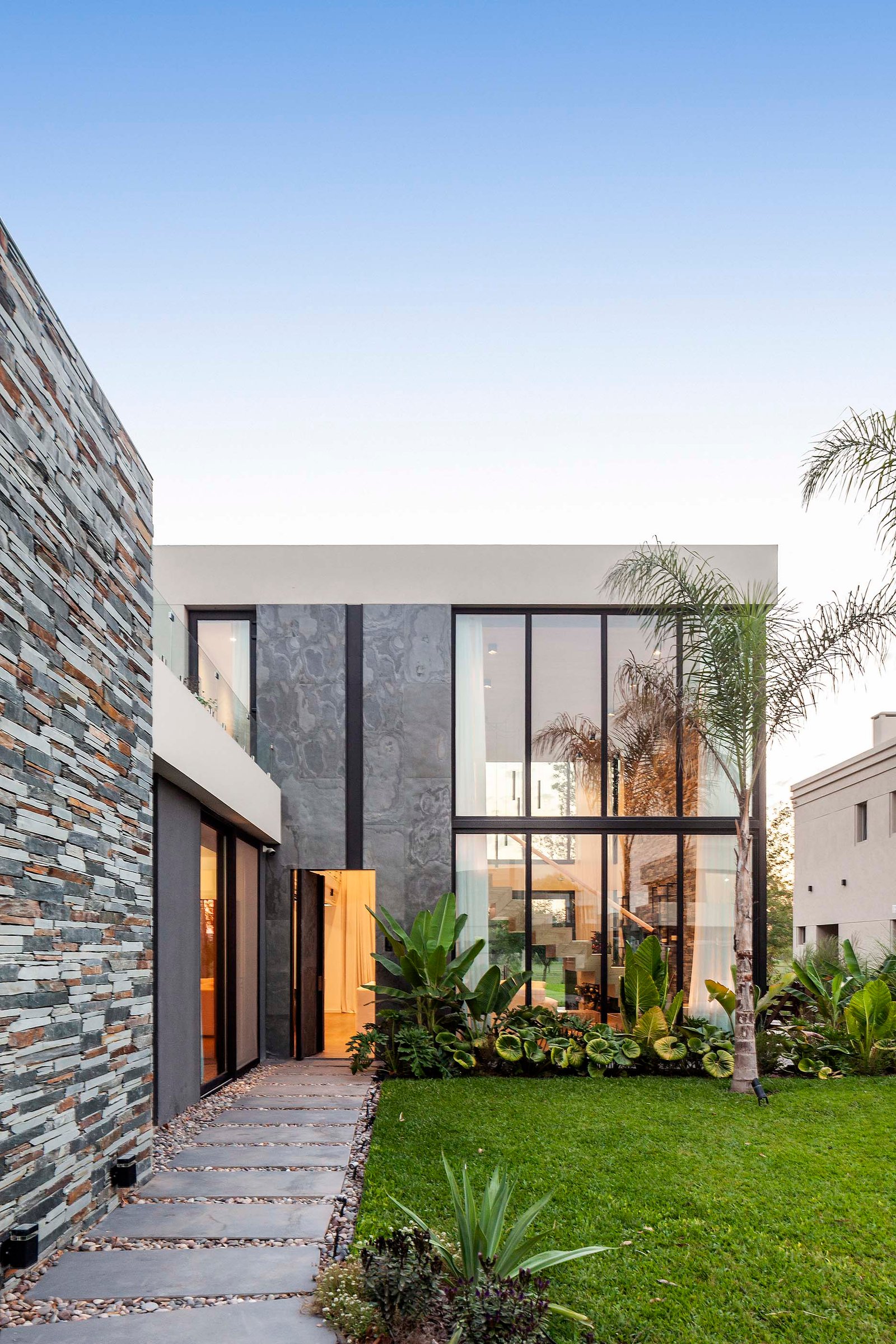 Fachada moderna con piedra apilada y ventanales de piso a techo — proyecto CASA T199, por A'PRIMA - Arquitectura Sustentable, en Los Robles 5901