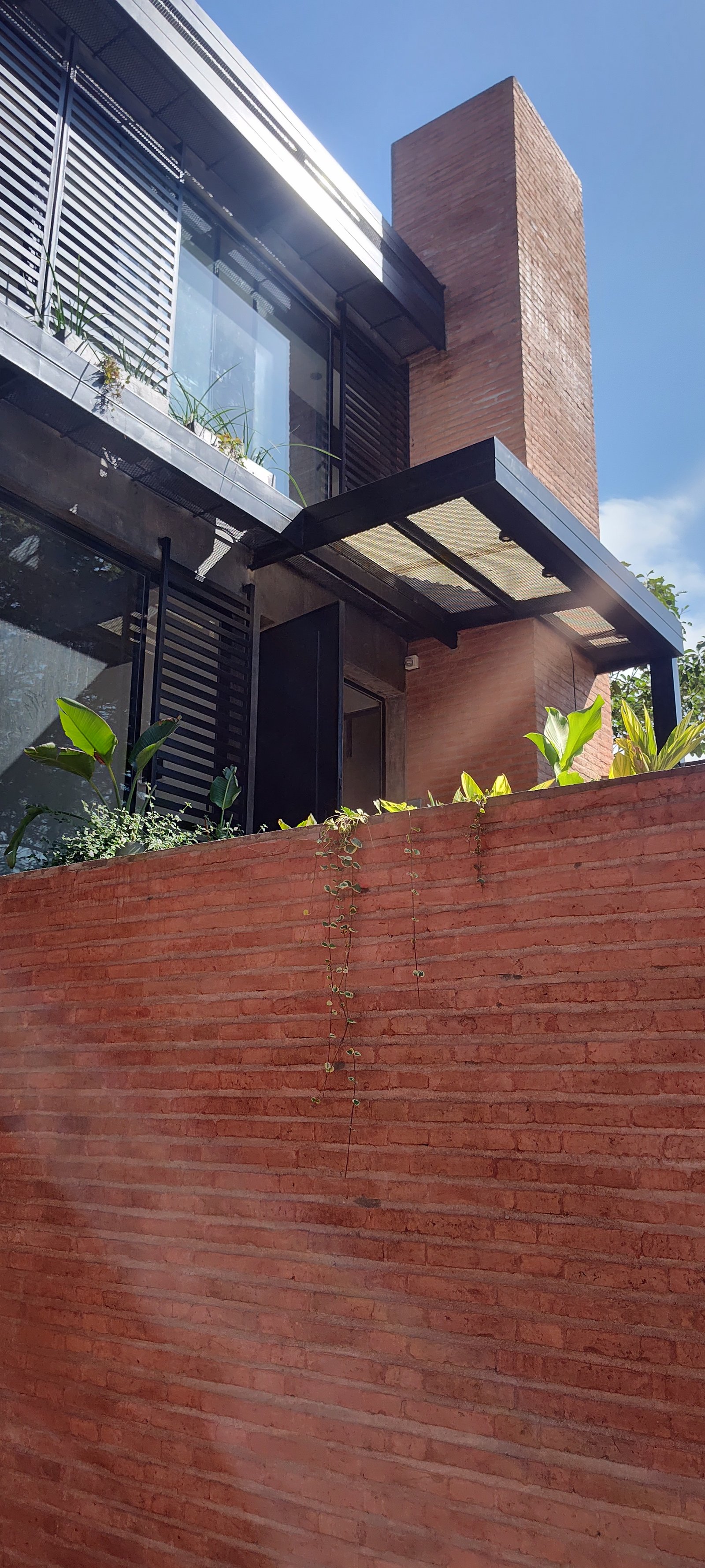 Fachada moderna em tijolo aparente terracota com vegetação — projeto GARDEN OFFICE, por HMCONSTRUCCIONES, em San Lorenzo 146