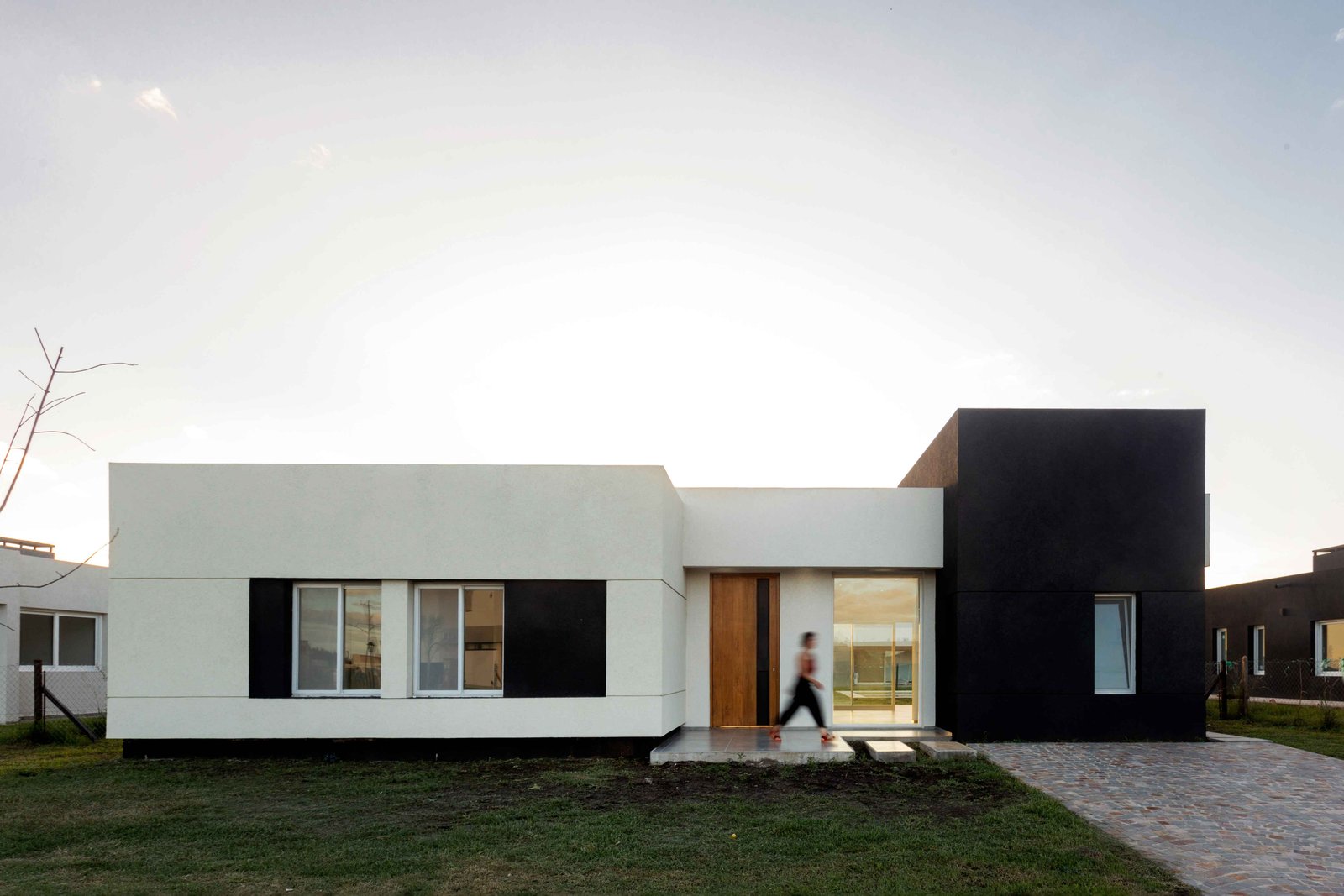 Fachada moderna preta e branca com pessoa caminhando — projeto San Simon I, por Estudio Stepa, em Ezeiza