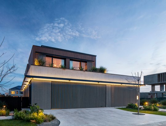 Fachada contemporánea nocturna con garaje y ventanales iluminados — proyecto Obra Wharehouse, por lifecycle, en B1648 Tigre