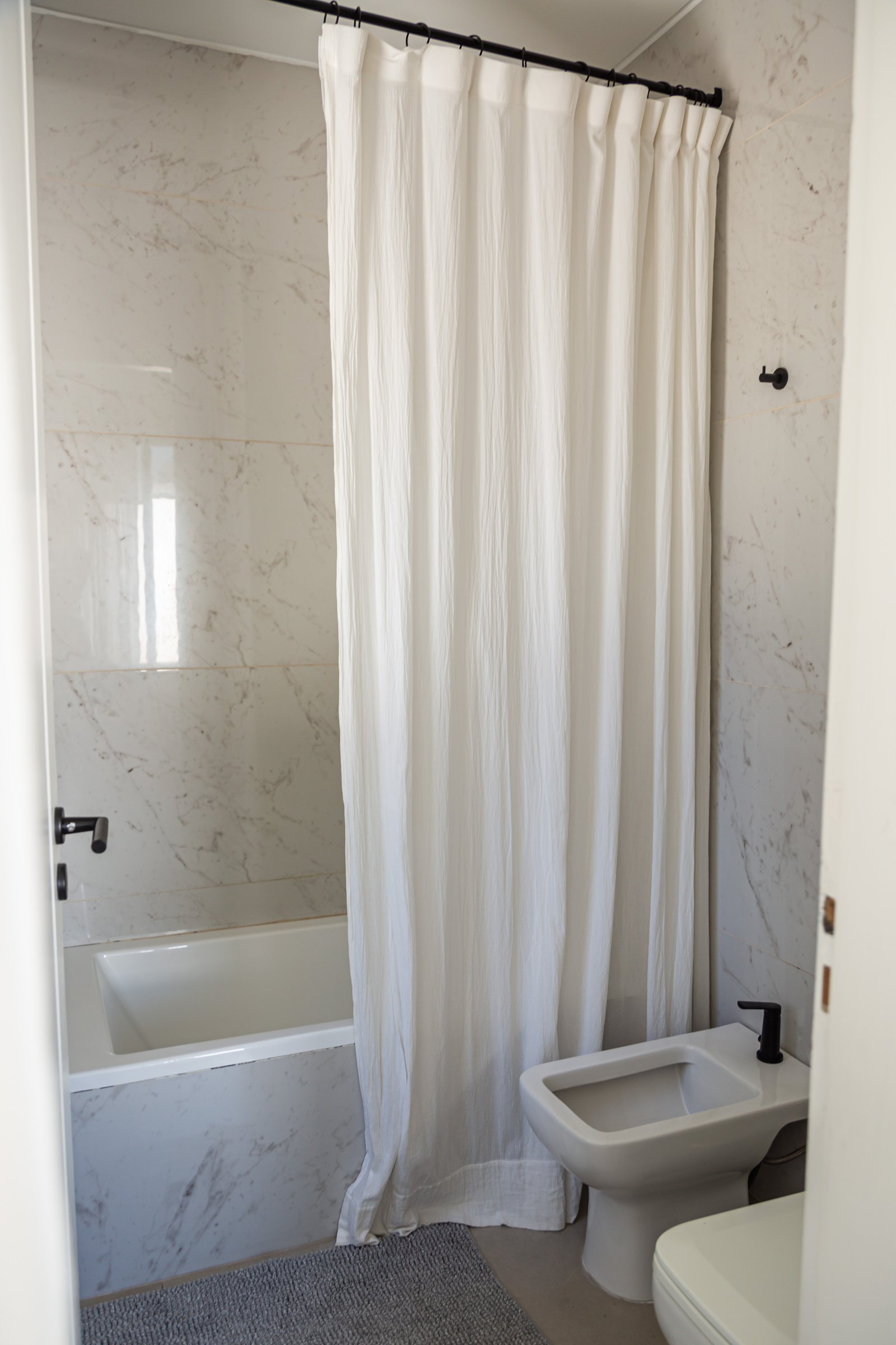 Baño moderno con bañera y bidet, paredes de mármol — proyecto CUBA 110, por Poce Arquitectura, en B1633 Fátima