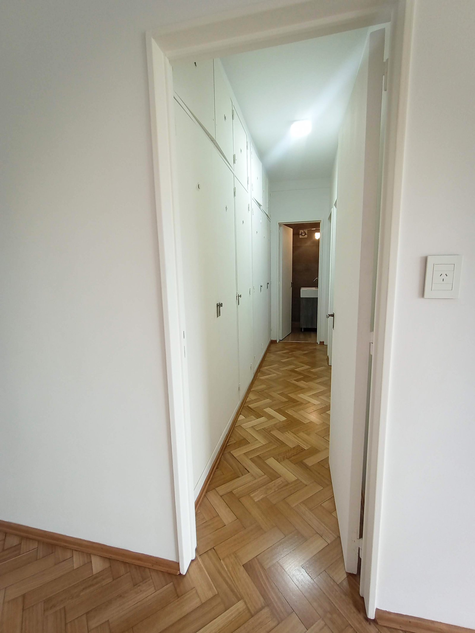 Pasillo blanco con suelo de madera en espiga y armarios empotrados — proyecto PH Beruti, por ASIA - arquitectura, en Palermo