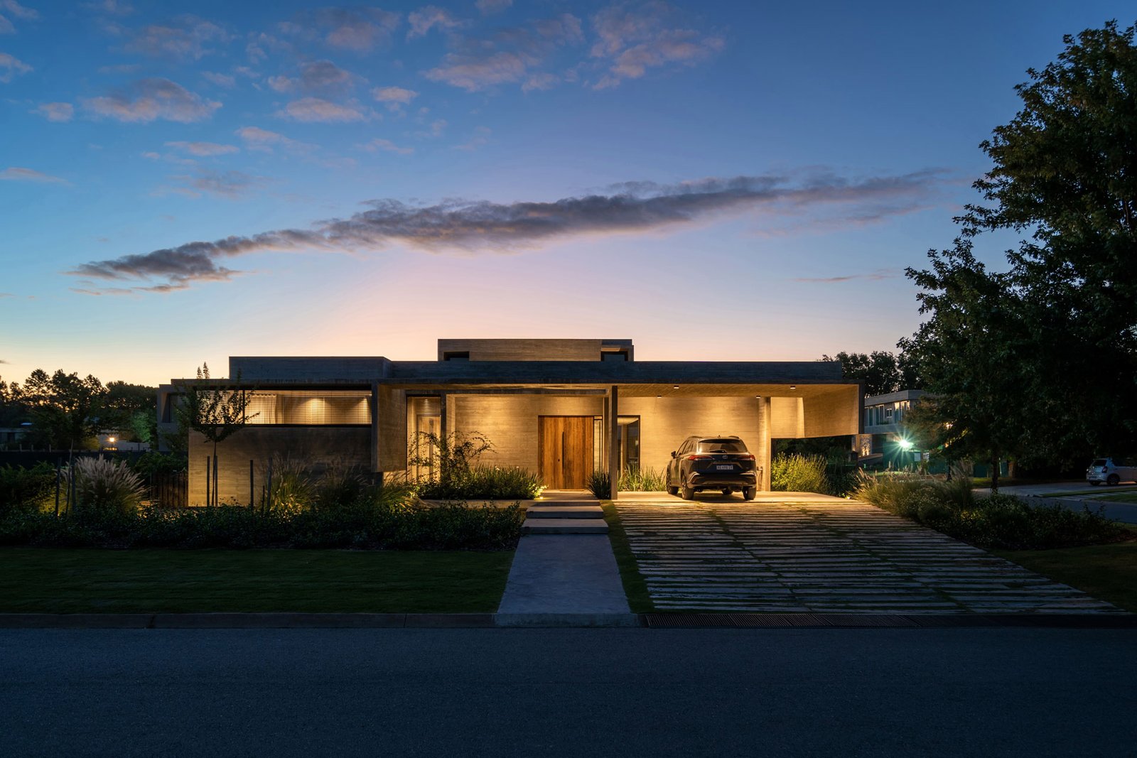 Fachada moderna de casa con madera y hormigón, iluminación cálida — proyecto Casa Tres Patios, por Besonías Almeida arquitectos, en Pilar