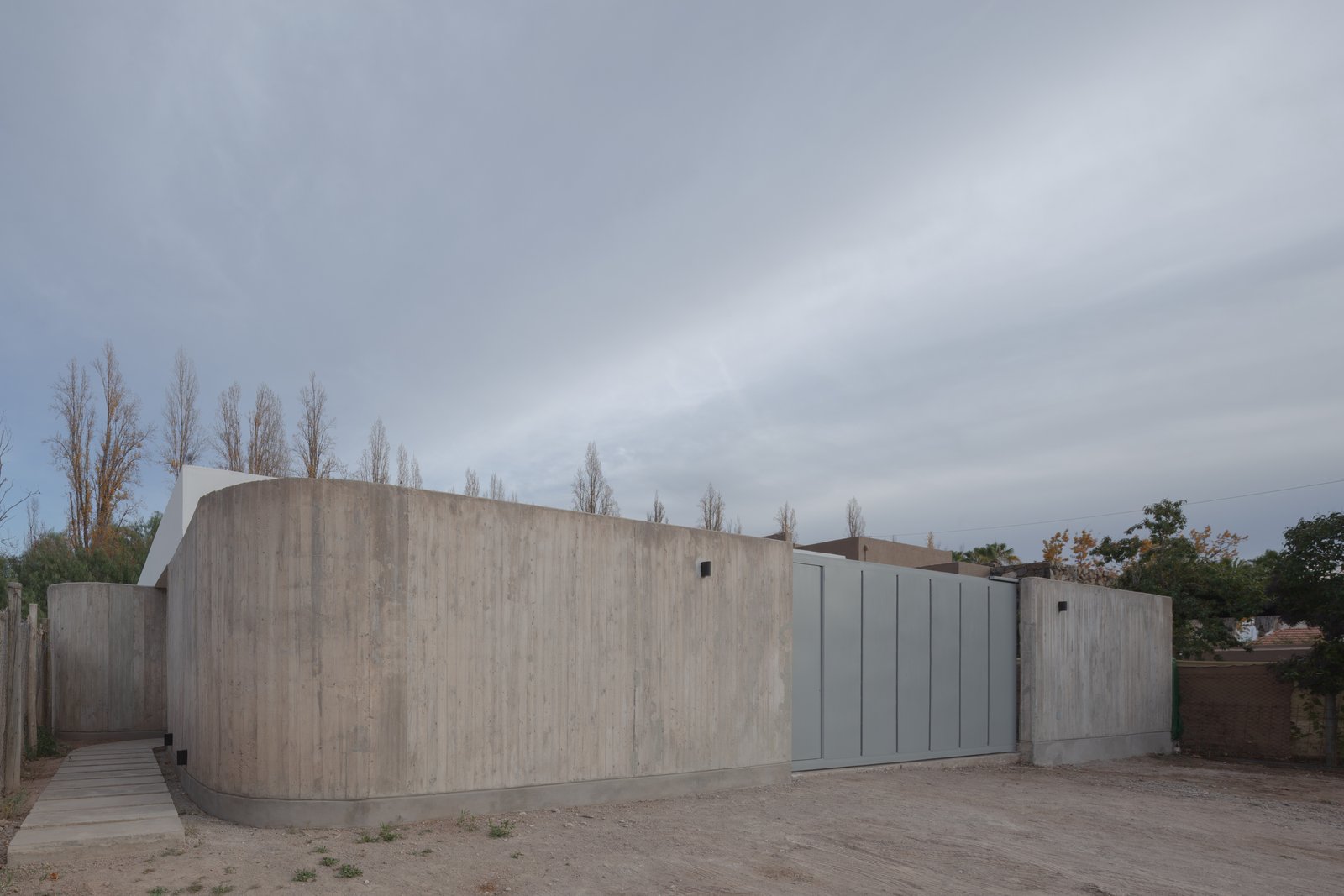 Fachada de casa moderna con muro curvo de hormigón — proyecto Vivienda CCE, por ONA - Oficina Nómada de Arquitectura, en M5505 Chacras de Coria