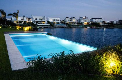 Piscina moderna iluminada por la noche con césped y casas de lujo — proyecto Casa Nordelta, por linearecta.arquitectura, en Nordelta