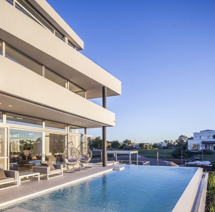 Piscina infinita y fachada moderna con sillas colgantes — proyecto Casa Caledoiscopio, por Apaarquitectura, en Nordelta