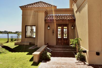 Fachada estilo mediterráneo con techos de teja y amplio jardín verde — proyecto San Marcos, por Marconi Silva Arquitectos, en Benavidez