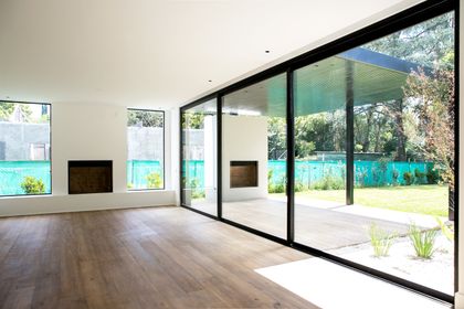 Sala de estar moderna con ventanales y jardines, piso de madera — proyecto Bosque Chico, por Estudio Arq. María Sioli, en Garin